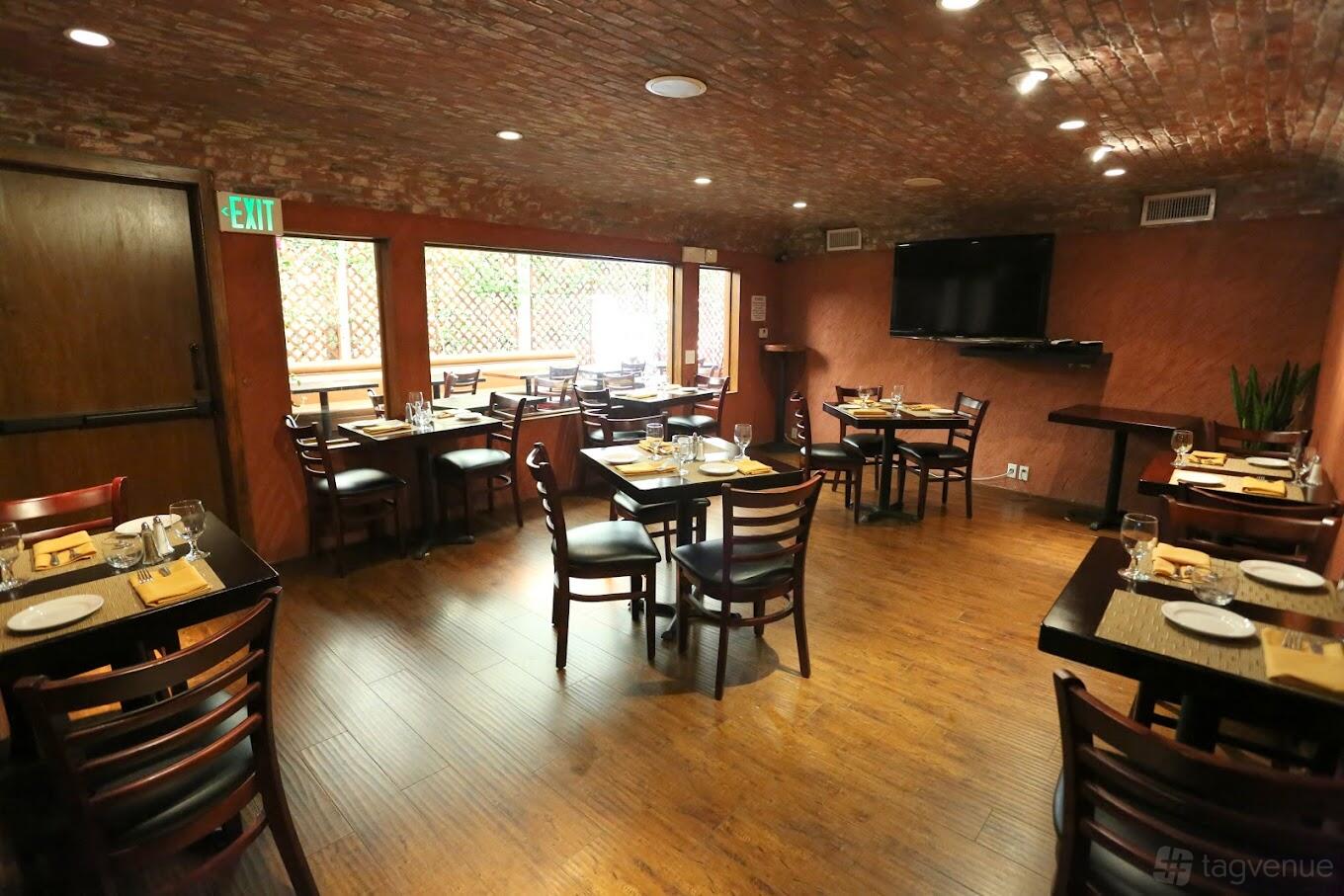 An event space in a restaurant with exposed brick ceiling, wood flooring, and dining tables at Bodega Malbec.