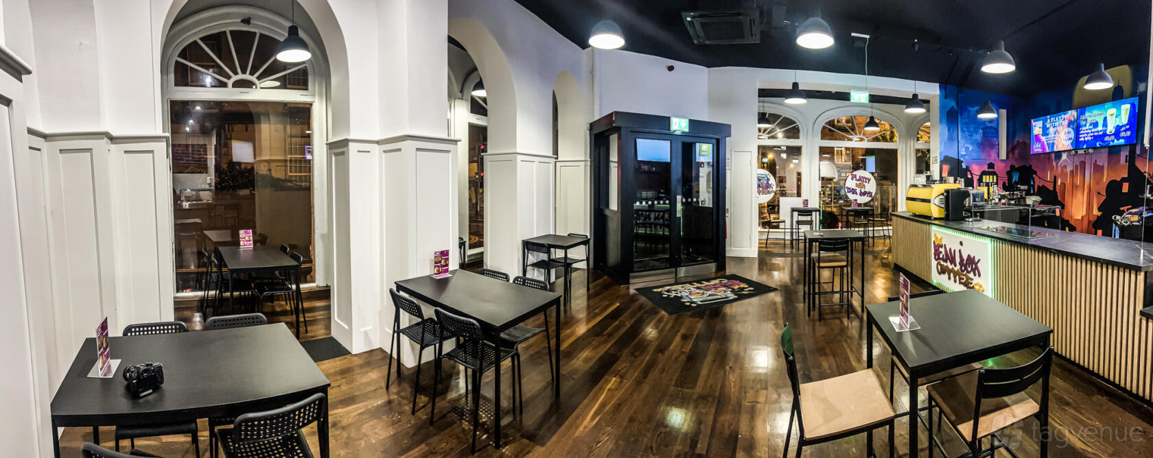 A cafe with arched windows, pendant lighting, and black tables on polished wood floors at The Bean Box.
