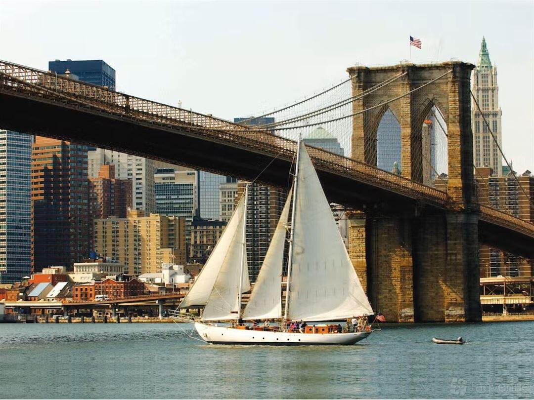 A classic sailing yacht with white sails cruising near the Brooklyn Bridge at Shearwater (Manhattan By Sail).