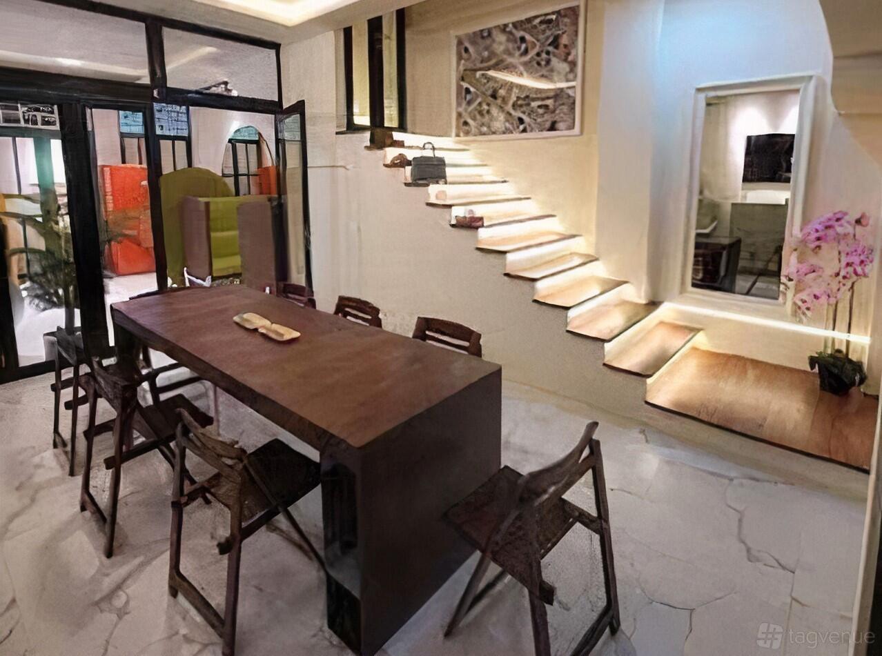 A dining room with a long wooden table, black chairs, marble flooring, and illuminated stairs at Petain Road.
