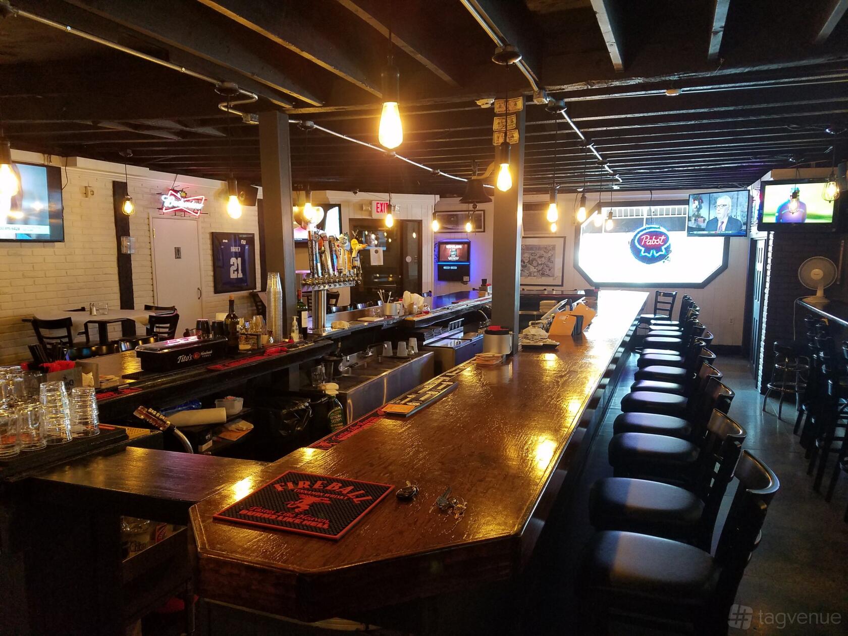 A bar with a wooden counter, draft beer taps, bar stools, and exposed ceiling beams at Bayonne Patio Bar & Grille.