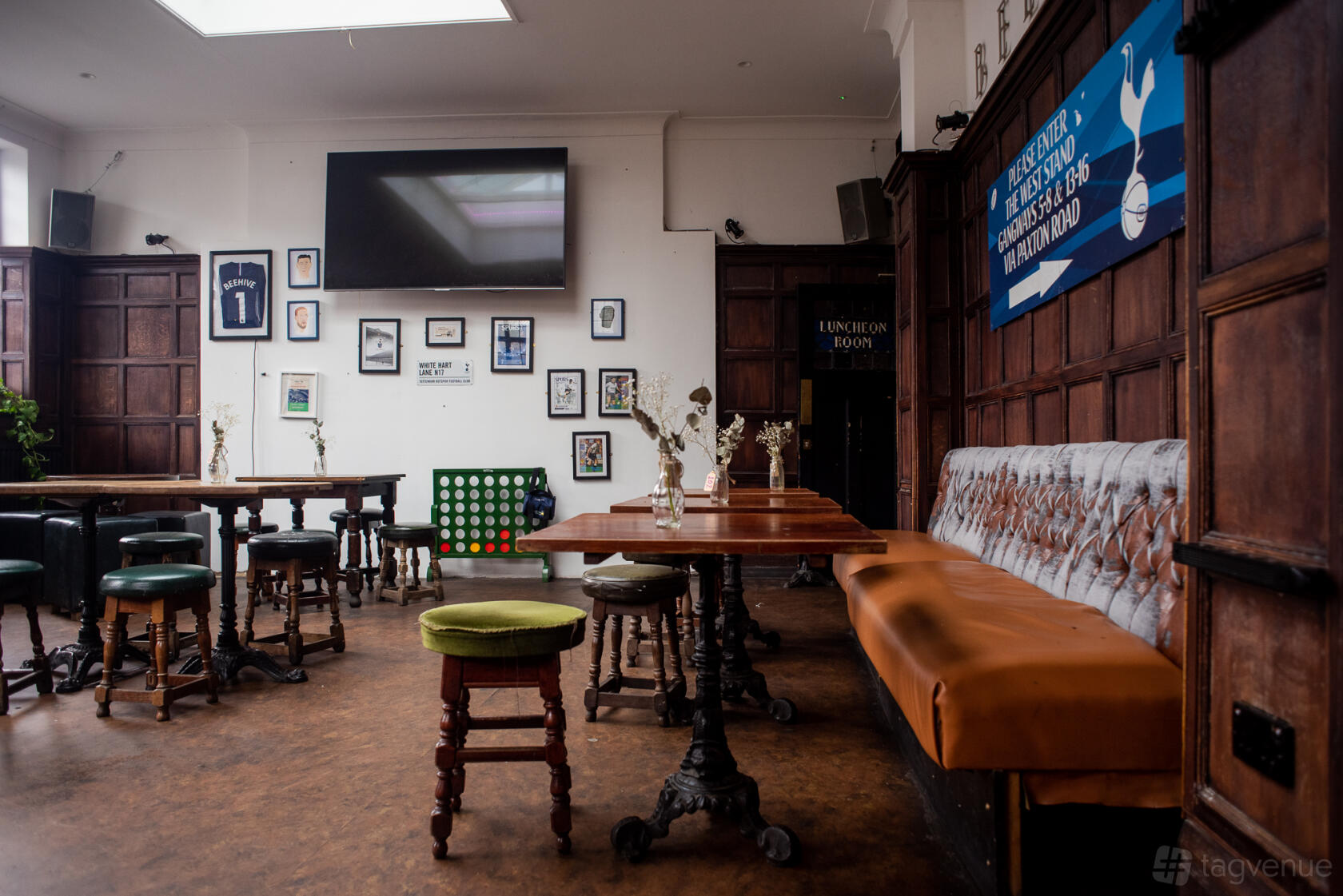 A dining room in a pub with wooden tables, upholstered bench seating, framed sports memorabilia, and a wall-mounted TV at The Beehive.