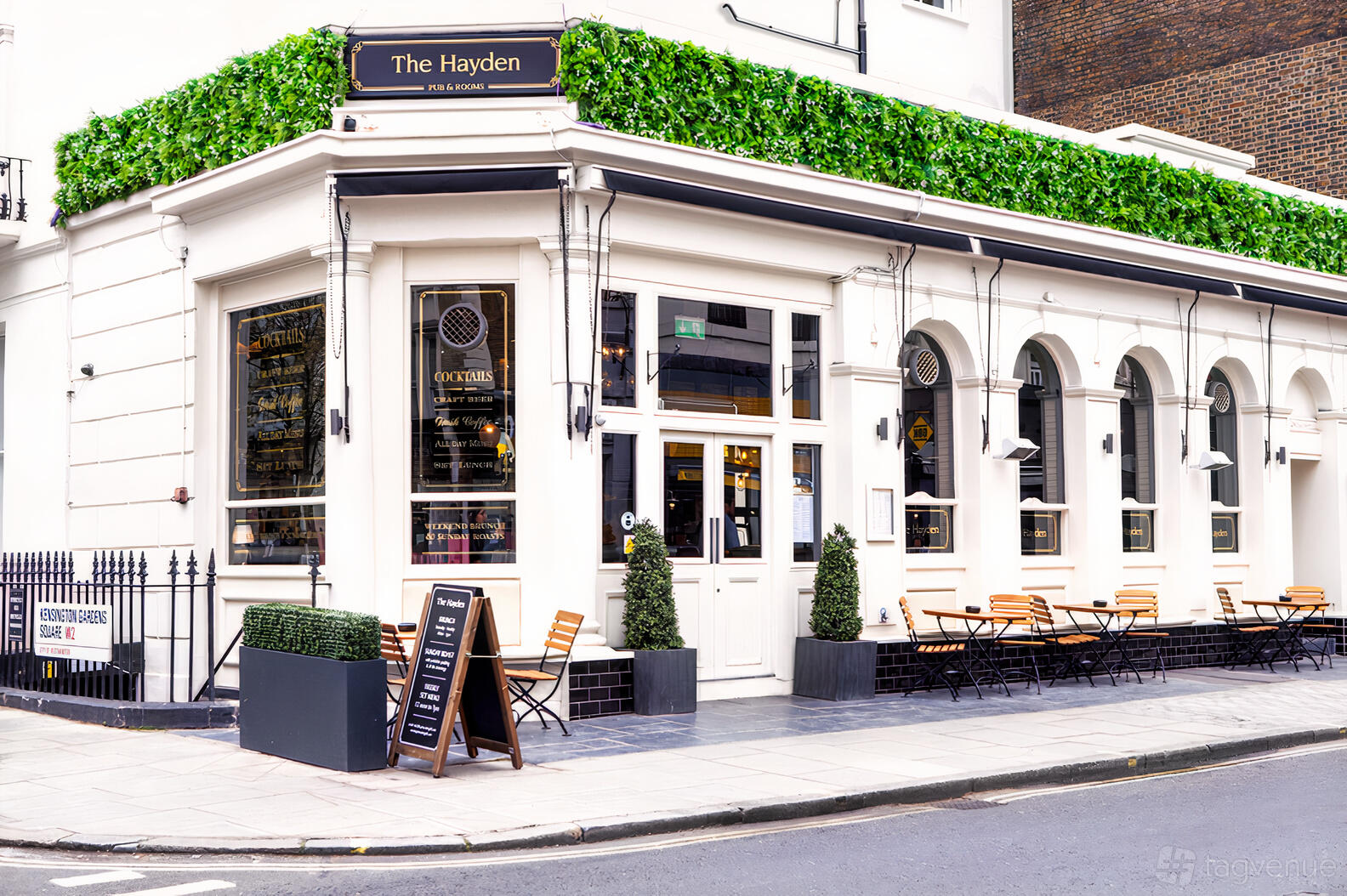 A corner restaurant with large arched windows, outdoor seating, and green wall accents at The Hayden.