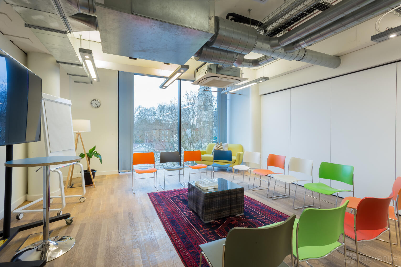 A meeting room with colorful chairs arranged in a circle, floor-to-ceiling windows, and exposed ductwork at Wallacespace Clerkenwell Green.