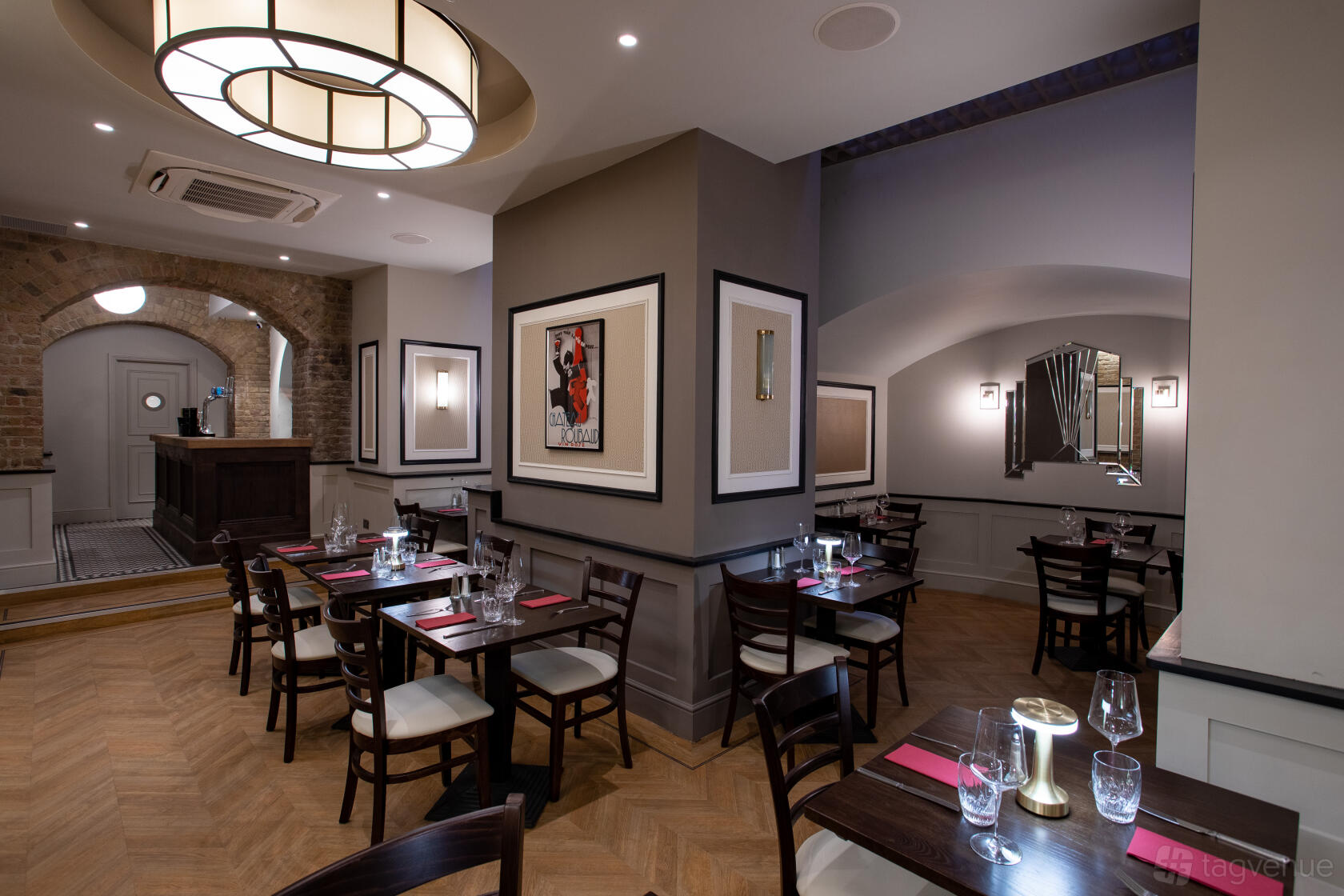 An event space in a bar with parquet floors, framed art, and wooden tables set with red placemats at Gigi's Bar Restaurant.