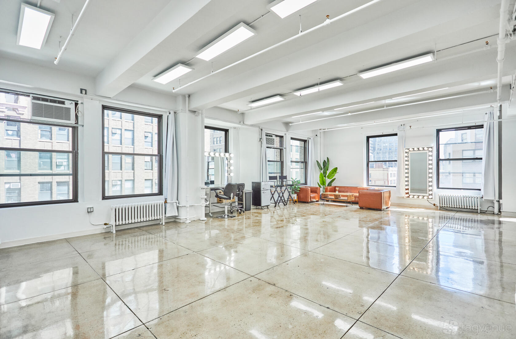 A photo studio with large windows, polished floors, makeup stations with lighted mirrors, and a brown sofa at Manhattan Skyline event space.