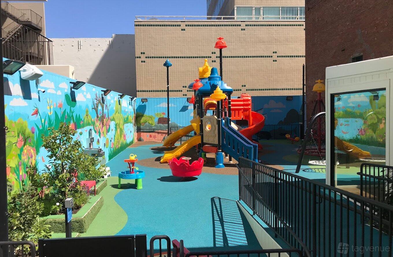 An outdoor playground with colorful climbing structures, slides, and mural walls at Seabird Preschool.
