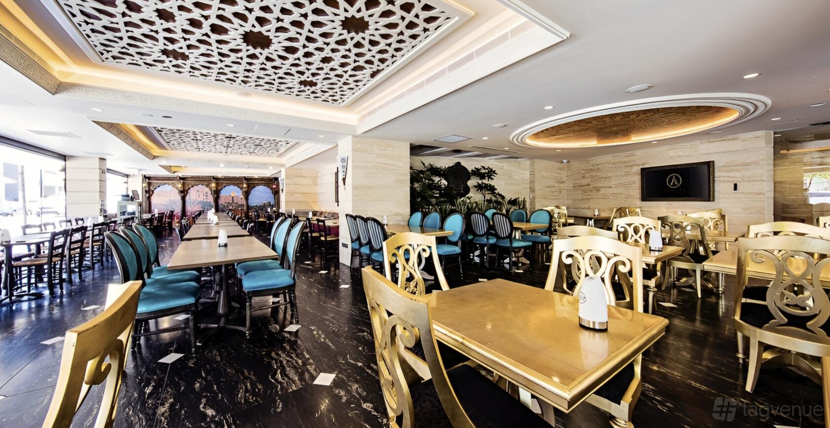 A restaurant dining room with gold-accented tables, blue upholstered chairs, patterned ceiling panels, and marble floors at Armani Restaurant.