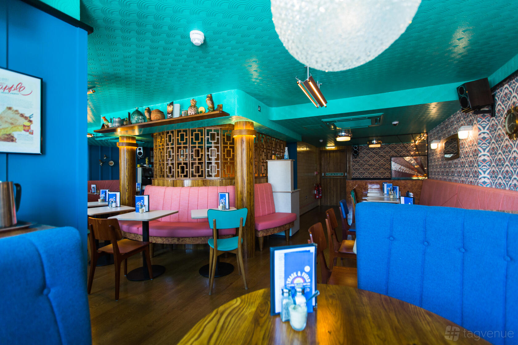 A colorful restaurant interior with teal ceiling, pink booth seating, wood tables, and patterned walls at The Breakfast Club Brighton.