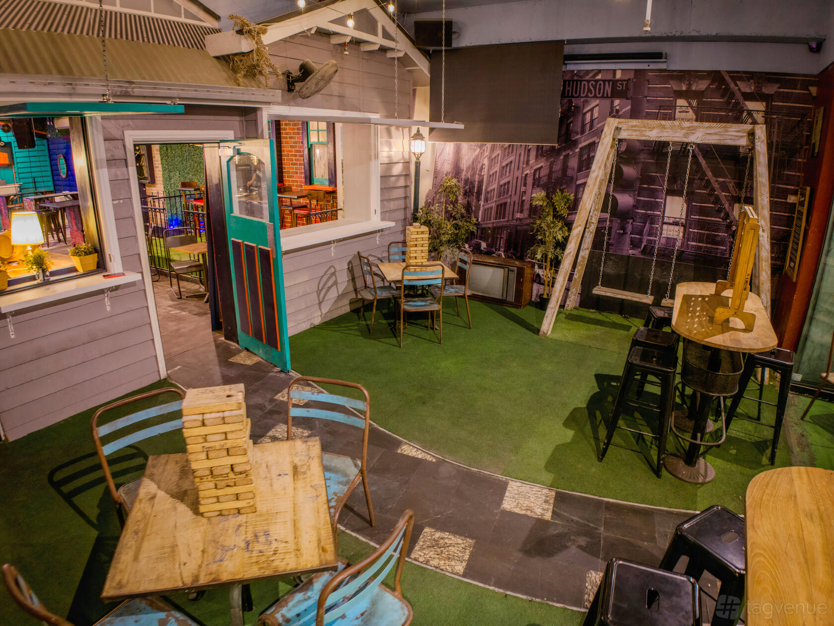 An event space with faux grass flooring, wooden tables, metal chairs, and a decorative porch swing at 29th Apartment — St Kilda.