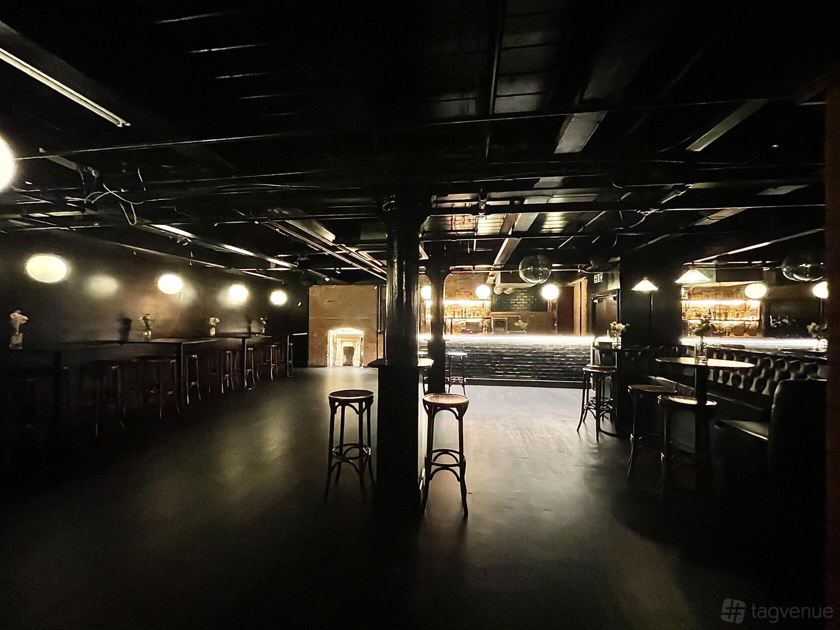 A dimly lit basement bar with round high tables, wooden stools, and a glowing backlit bar at The Whiskey Jar.