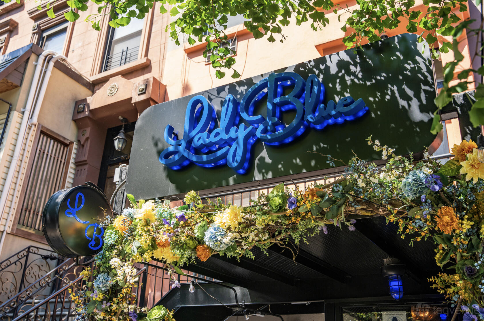 A pub with a blue neon sign, floral garland, and black awning at Lady Blue