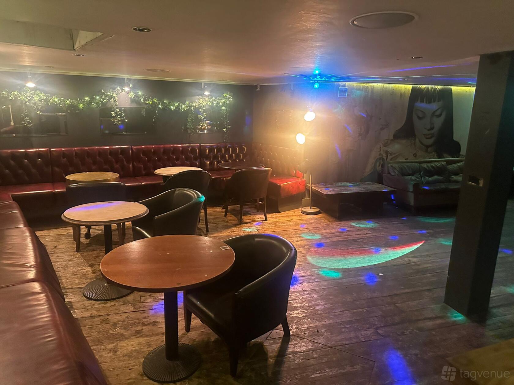 A function room in a pub with leather banquette seating, round wooden tables, and disco lights at The Regent.