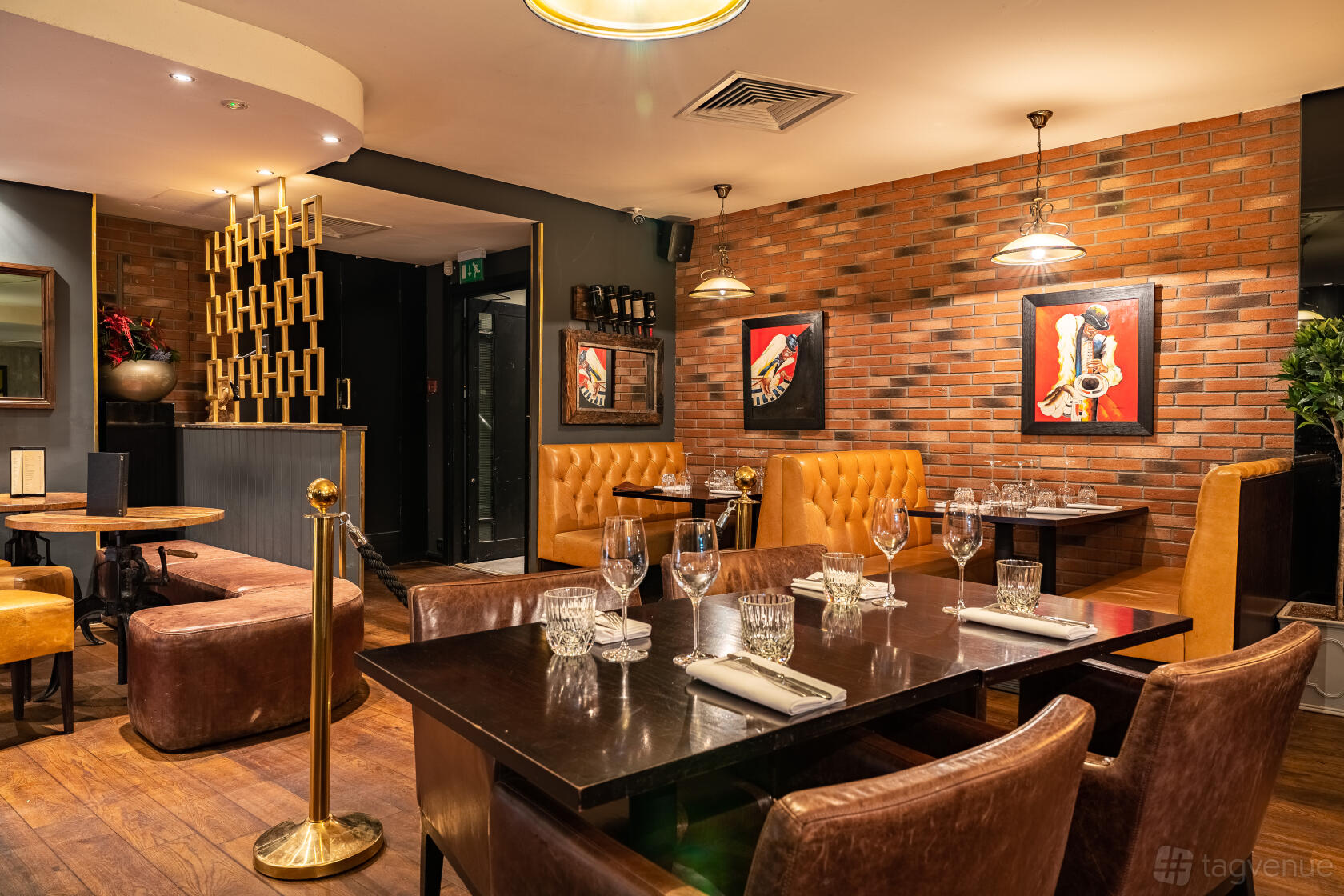 A restaurant with exposed brick walls, leather banquette seating, and set tables with glassware at Omnino Steakhouse.