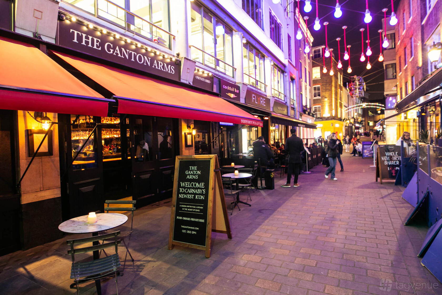A bar with outdoor seating, red awnings, and colorful overhead lights at The Ganton Arms.