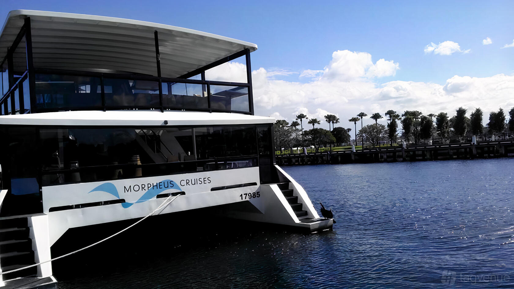 A modern boat with two open-air decks and glass-paneled railings docked at Morpheus Cruises.
