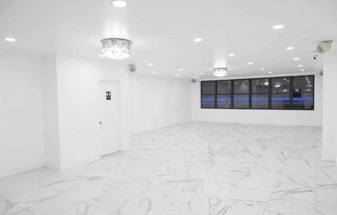 A function room with white marble flooring, crystal chandeliers, and large windows at Prime143.