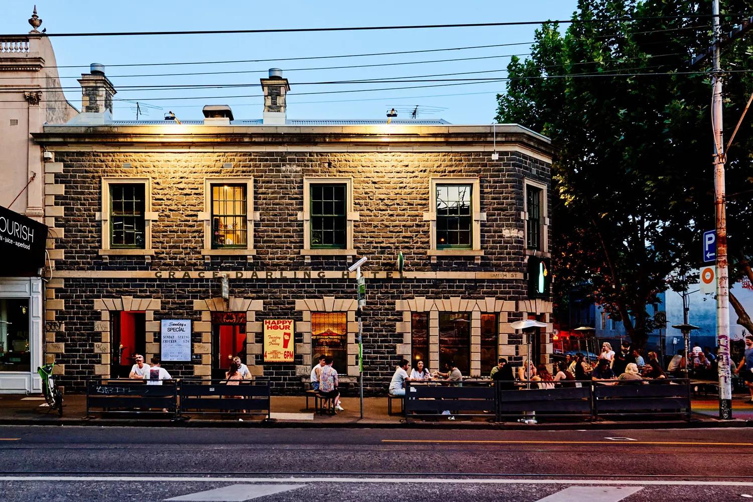 A pub with a bluestone facade, large windows, and outdoor seating on the sidewalk at The Grace Darling Hotel.