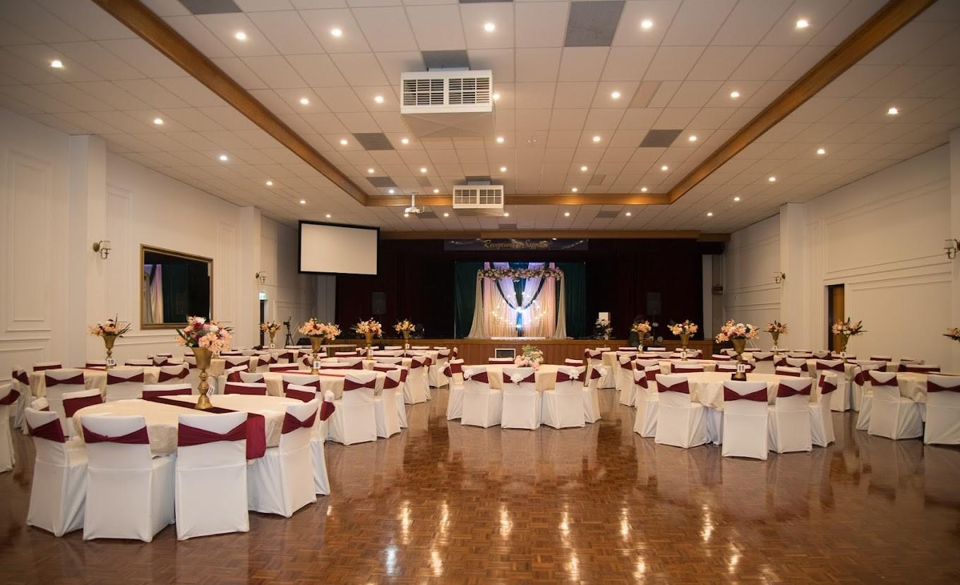 An event venue with round tables covered in white linens and burgundy chair sashes, stage with draping at Receptions At Sapphire