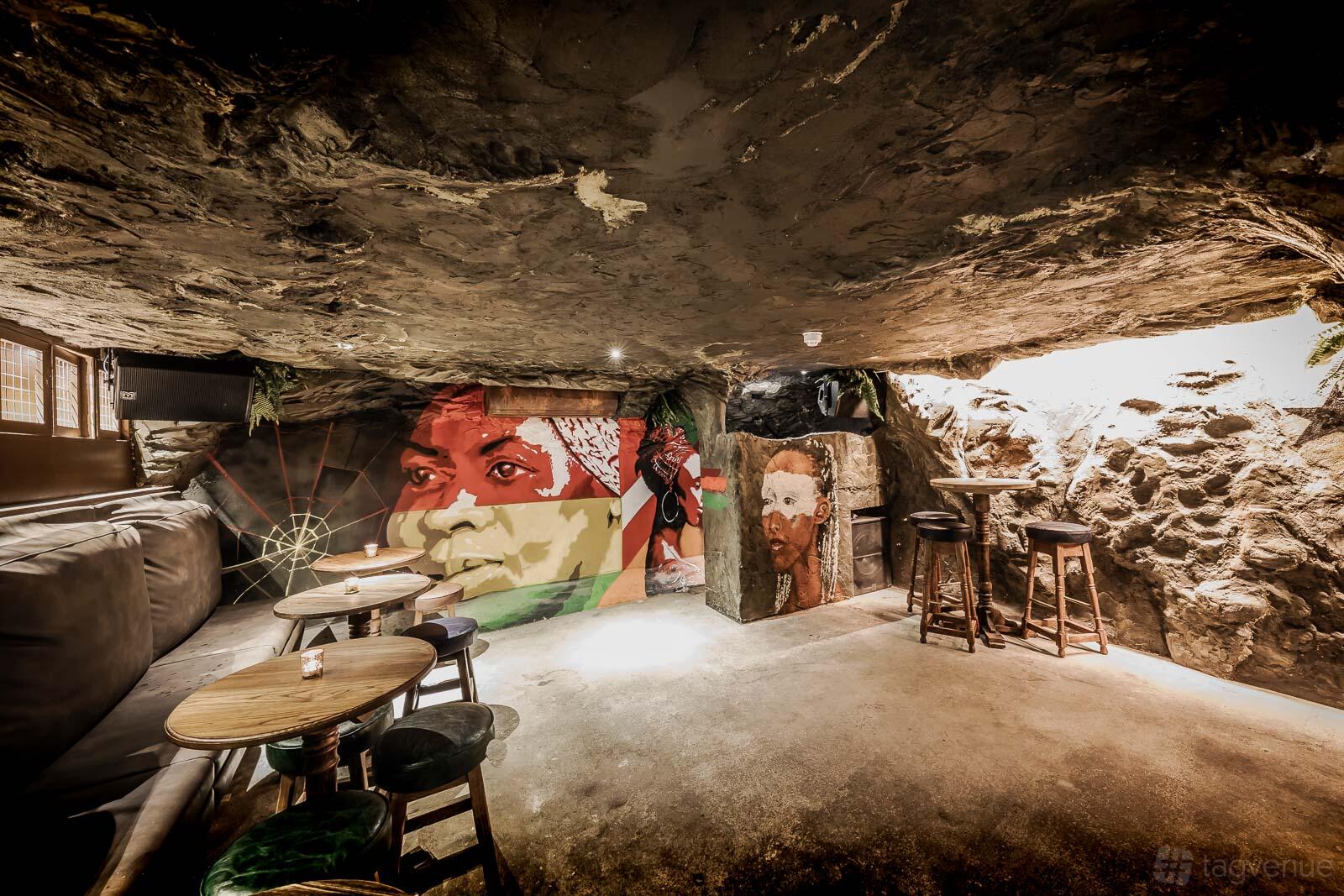 An event space in a pub with a rocky cave ceiling, mural art, and round wooden tables at Queen of the South.