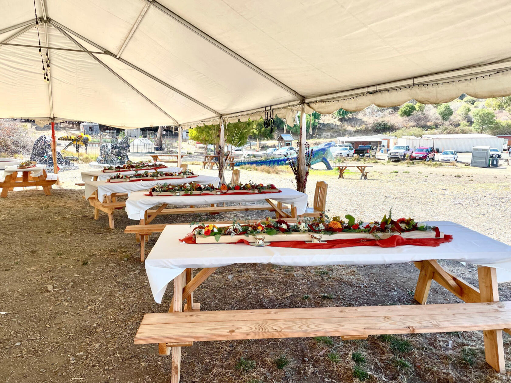 An outdoor event venue with long wooden picnic tables covered in white linens and floral centerpieces at Point San Pablo Harbor.