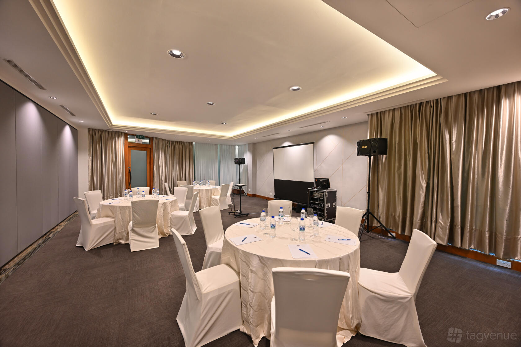 An event venue with round tables covered in white linens, beige curtains, and ceiling spotlights at Seletar Country Club.