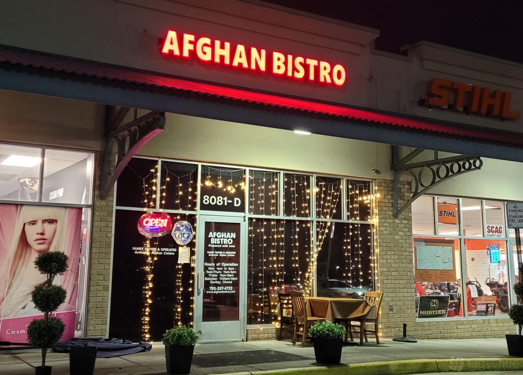 A restaurant with string lights on the front windows, a glass storefront, and a small outdoor table at Afghan Bistro.
