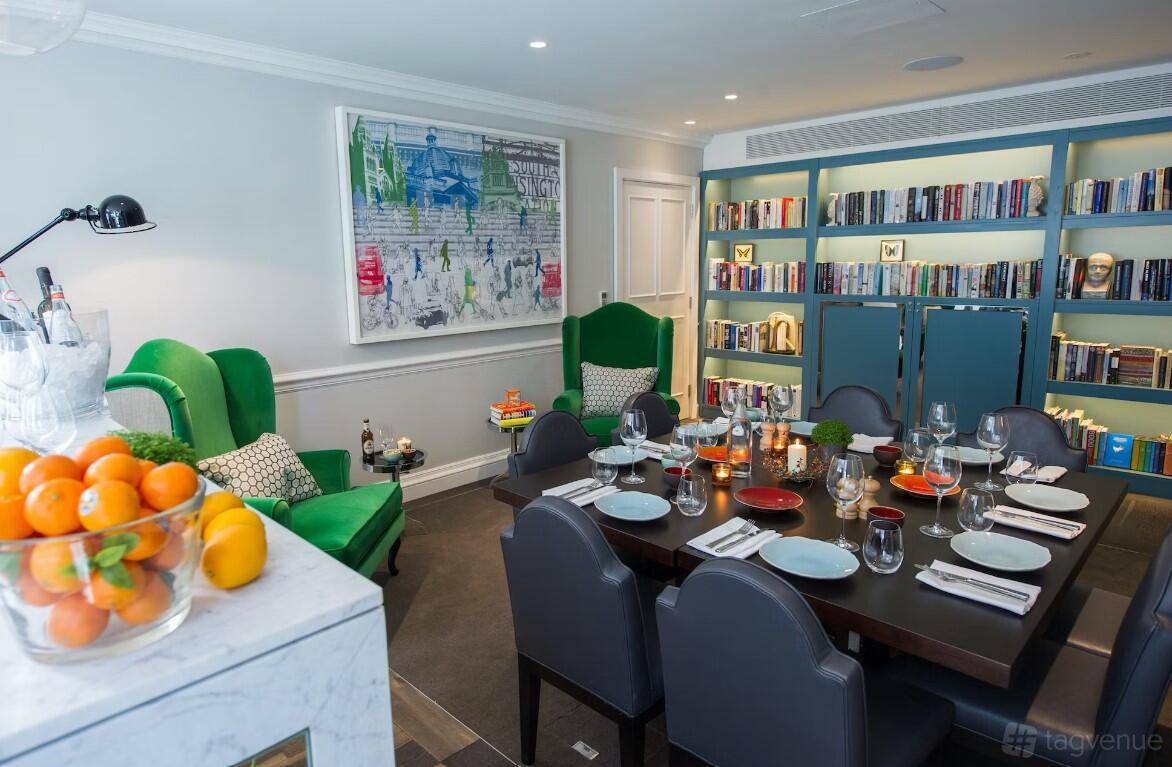 A hotel function room with bookshelves, green armchairs, and a dining table set for eight at The Ampersand Hotel.