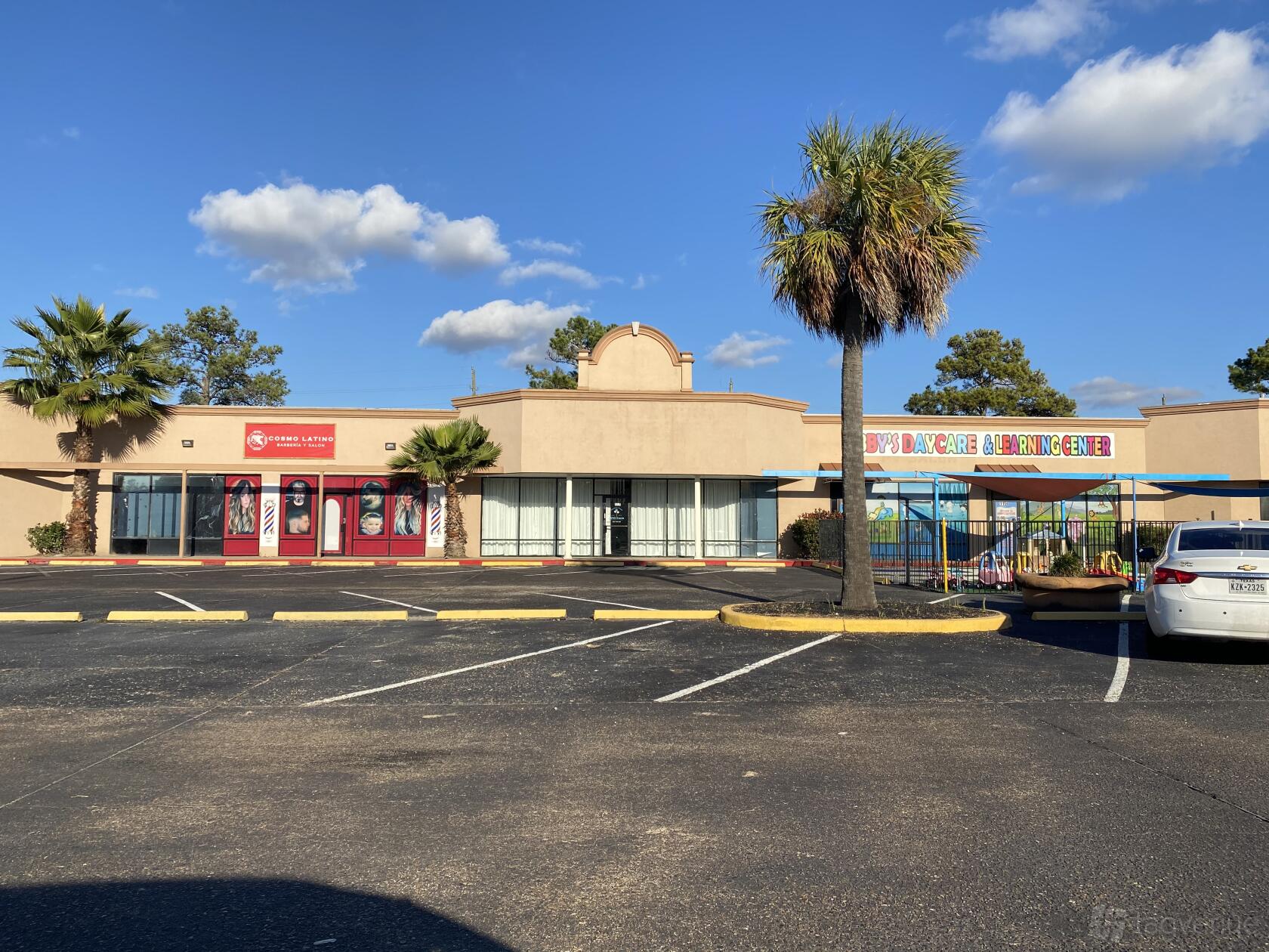 A hall with a tan facade, red entrance doors, and palm trees in the parking lot at Mins Events 117.
