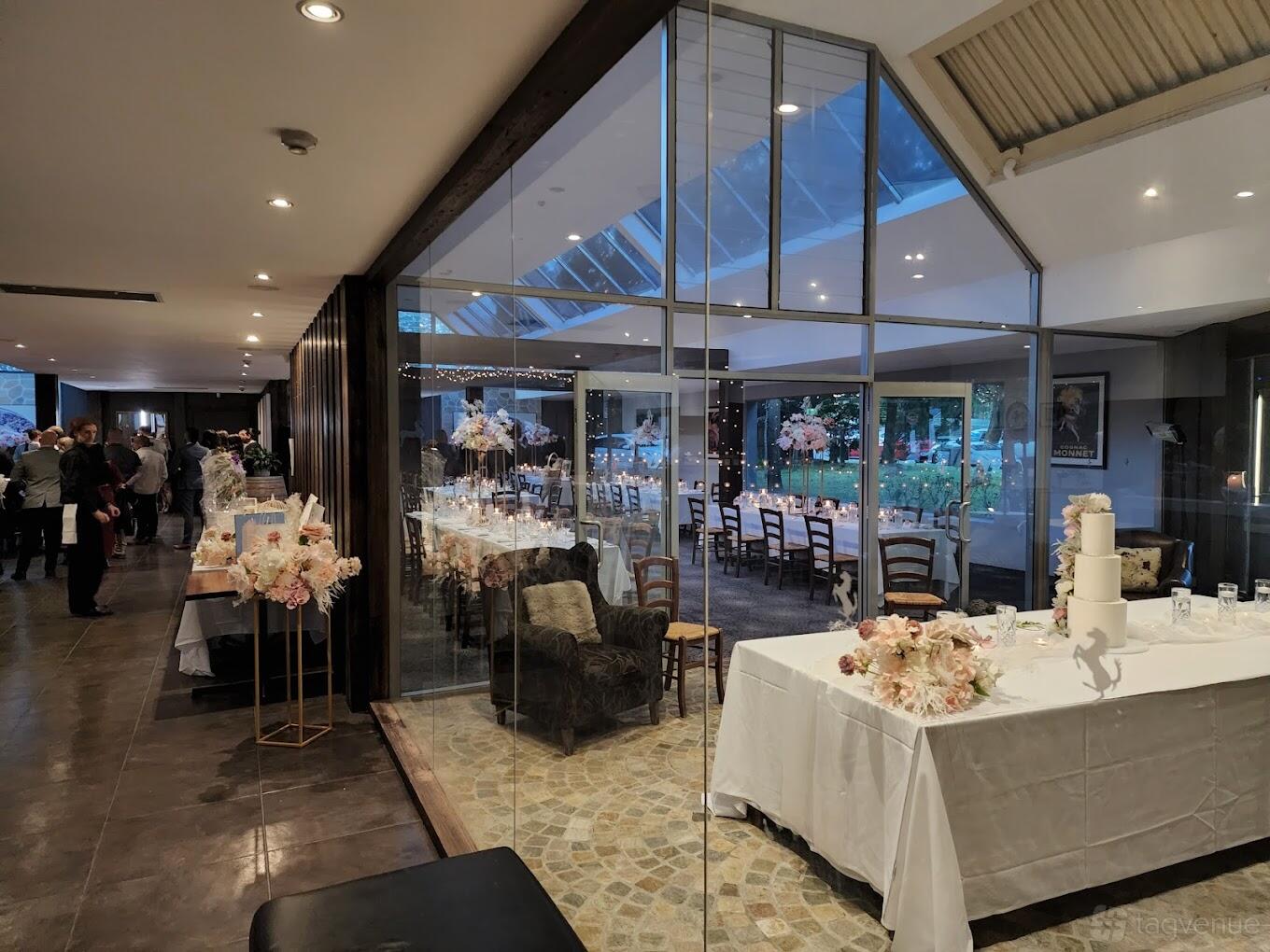 A restaurant with floor-to-ceiling glass walls, banquet tables with floral centerpieces, and warm lighting at Cavallino.