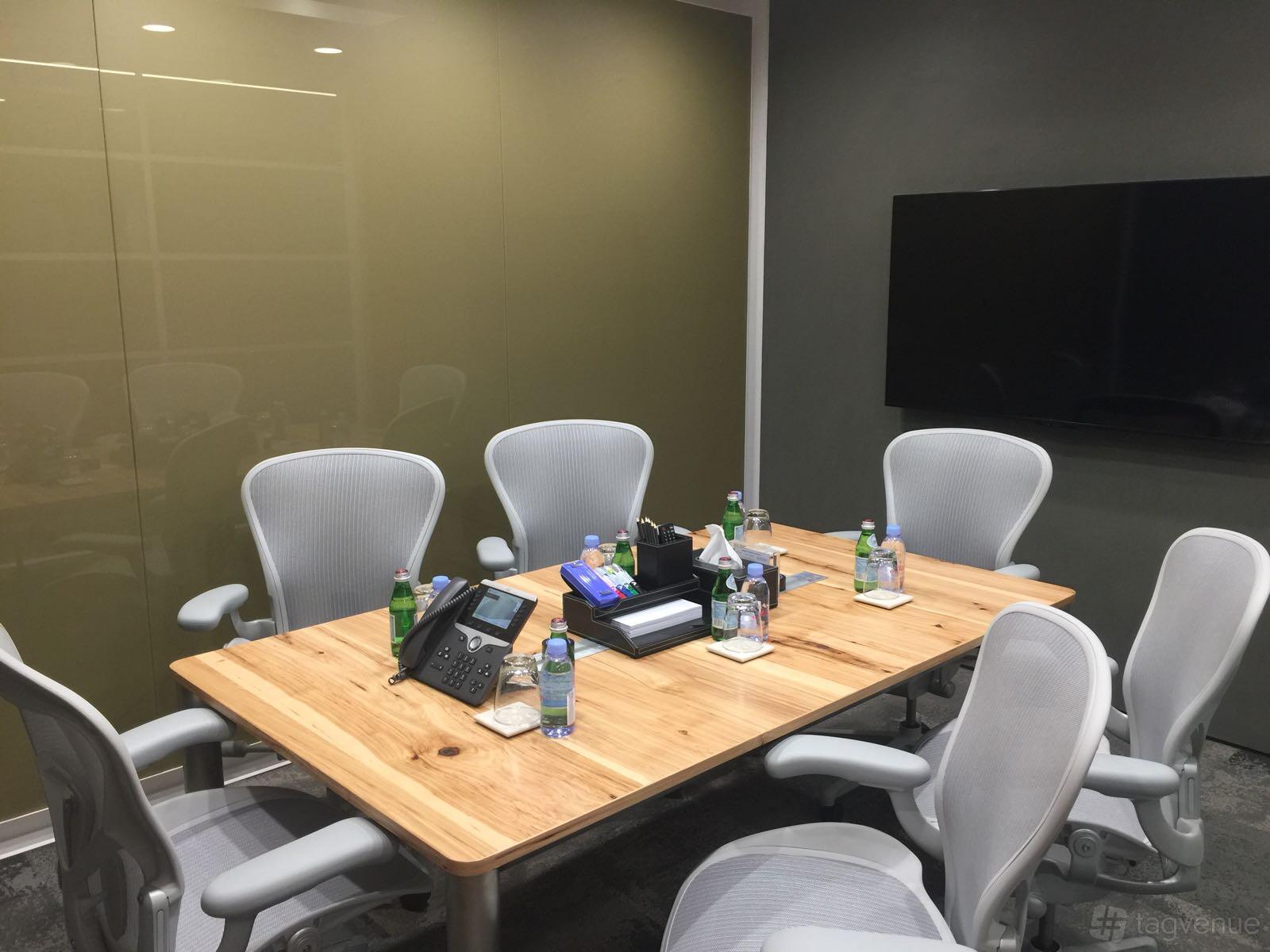 A meeting room with a wooden conference table, grey chairs, bottled water, and a wall-mounted screen at The Gateway West.
