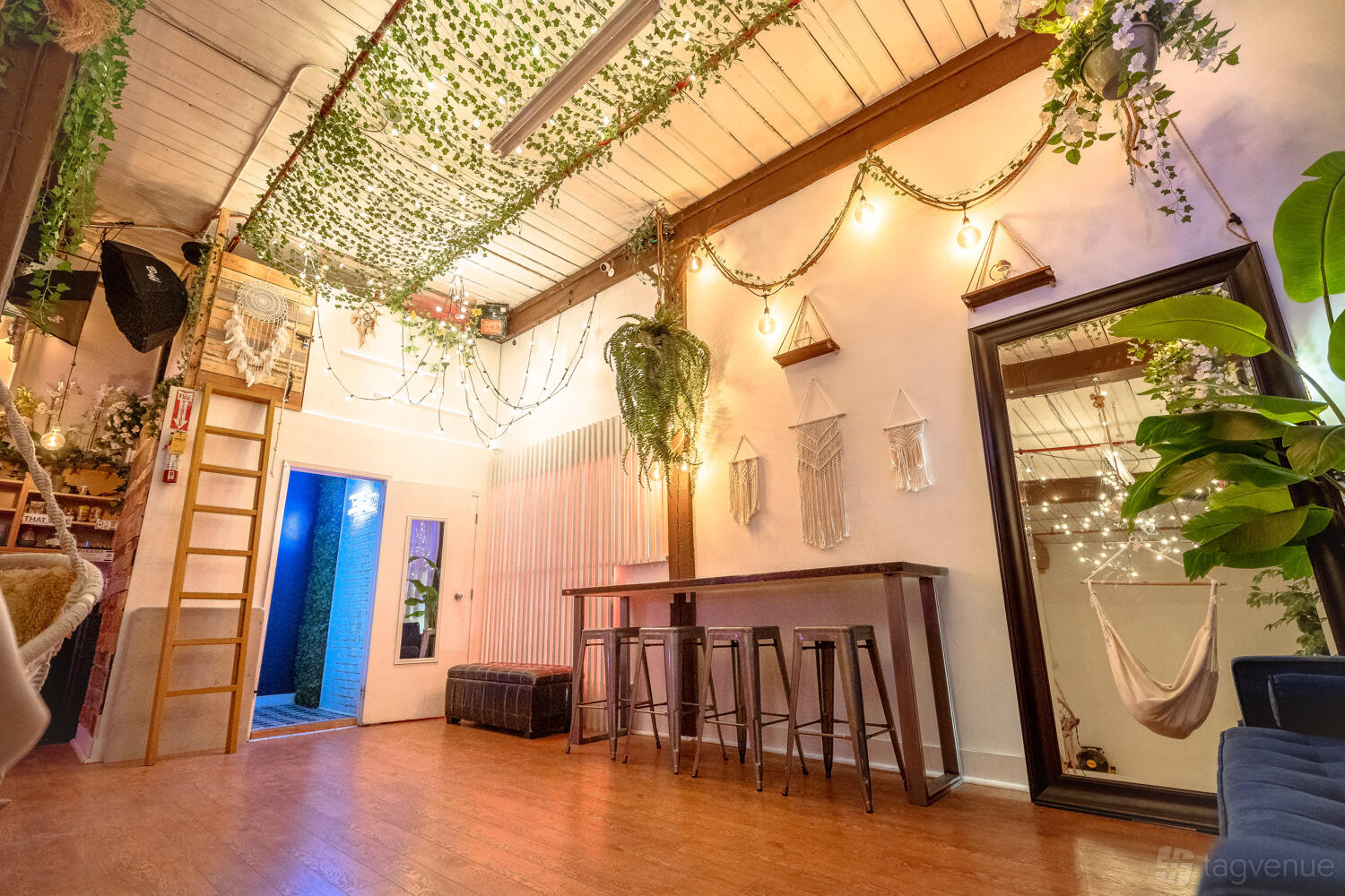 A loft with hanging greenery, string lights, wooden floors, and tall mirrors at Daylight Studio for Photos, Events, Meetings.