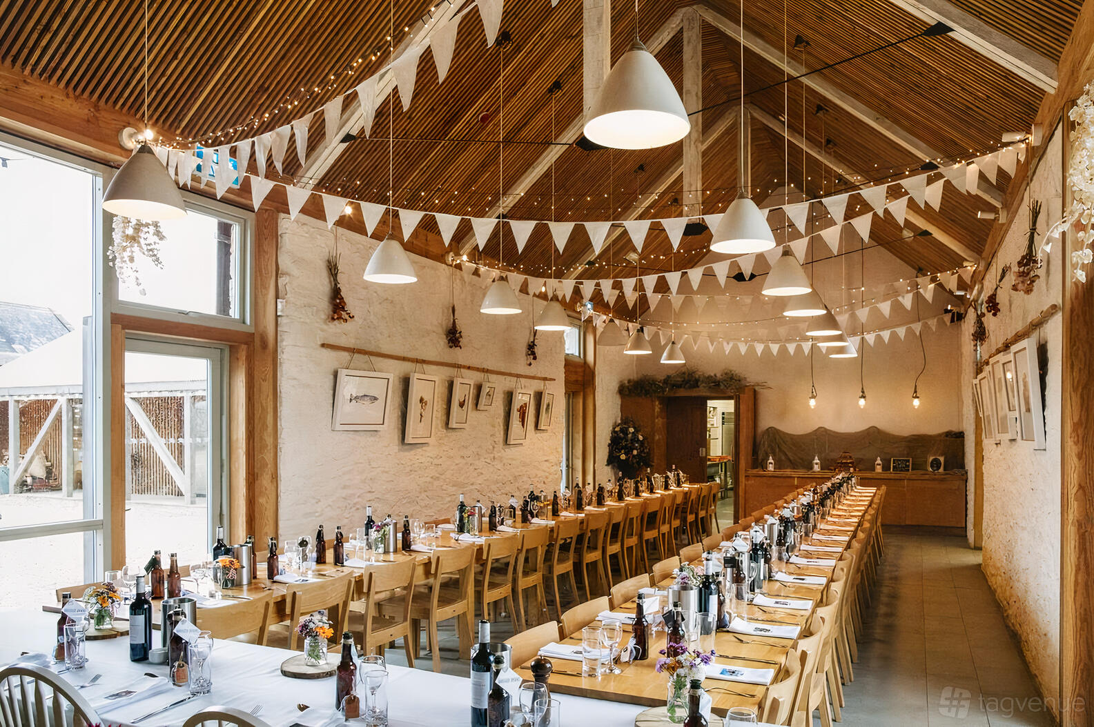 An event venue with long banquet tables, wooden chairs, bunting, and high beamed ceilings at River Cottage.