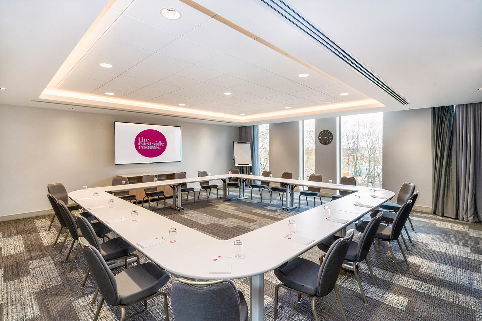 A conference room with U-shaped tables, presentation screen, and floor-to-ceiling windows at The Eastside Rooms.
