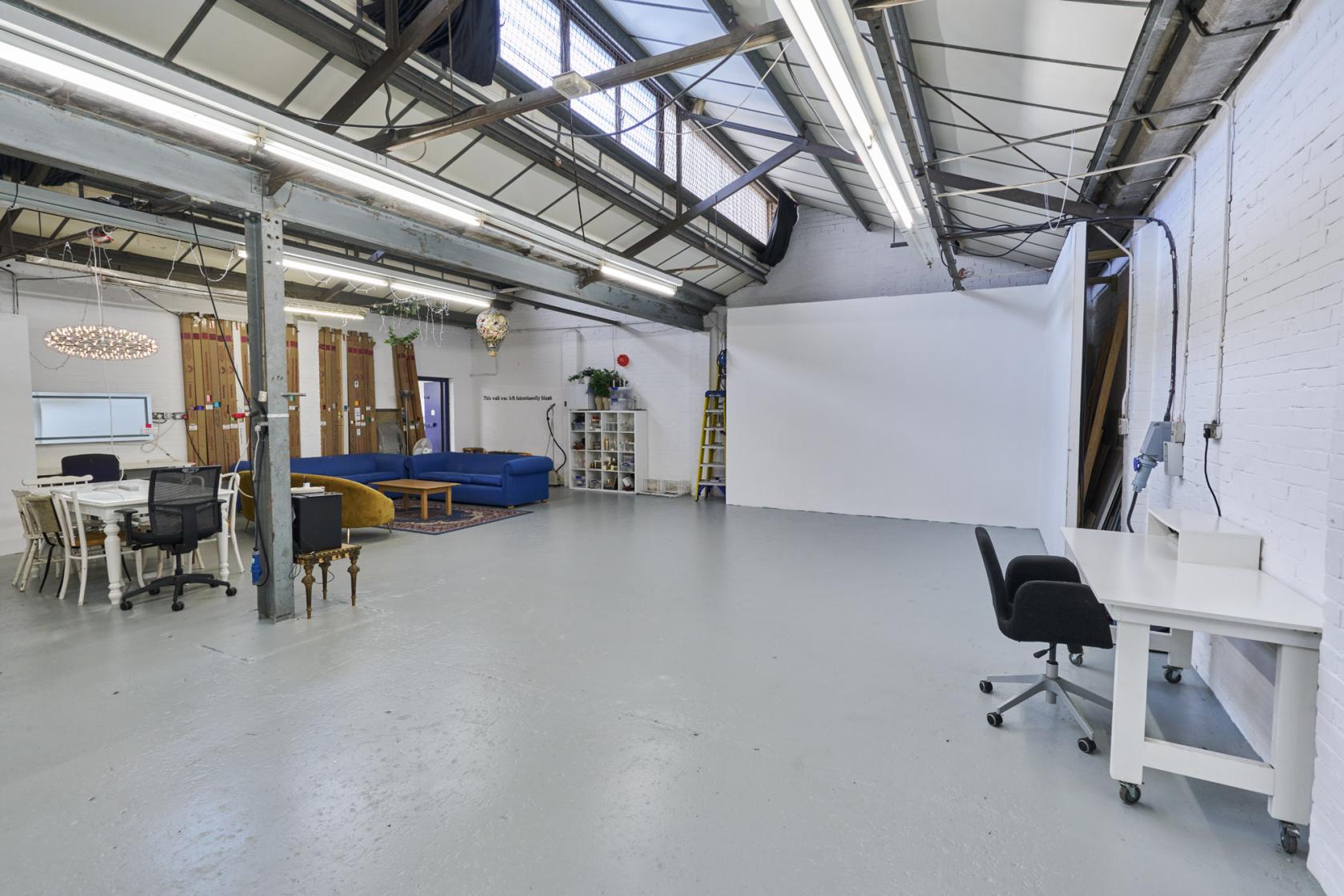 A photo studio with a large white cyclorama wall, exposed beams, skylights, and lounge seating at Bourbon Studio.