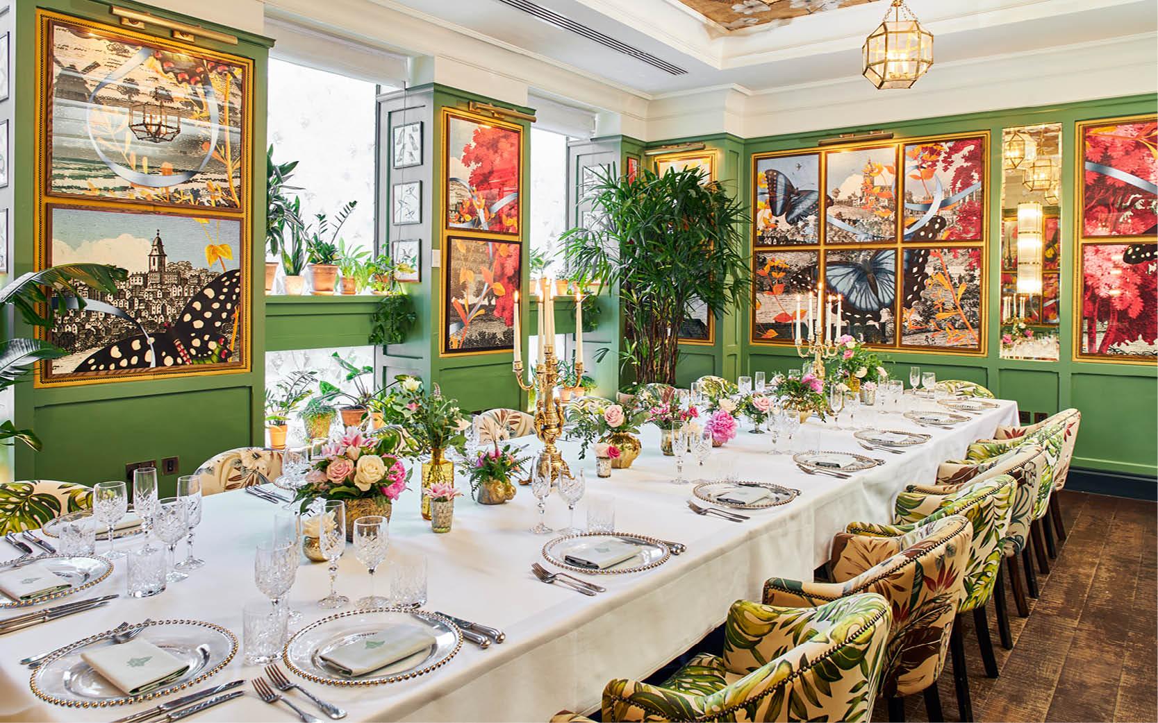 A dining room with floral-upholstered chairs, framed botanical art, candelabras, and a long table with white linens at The Ivy Temple Row Birmingham.