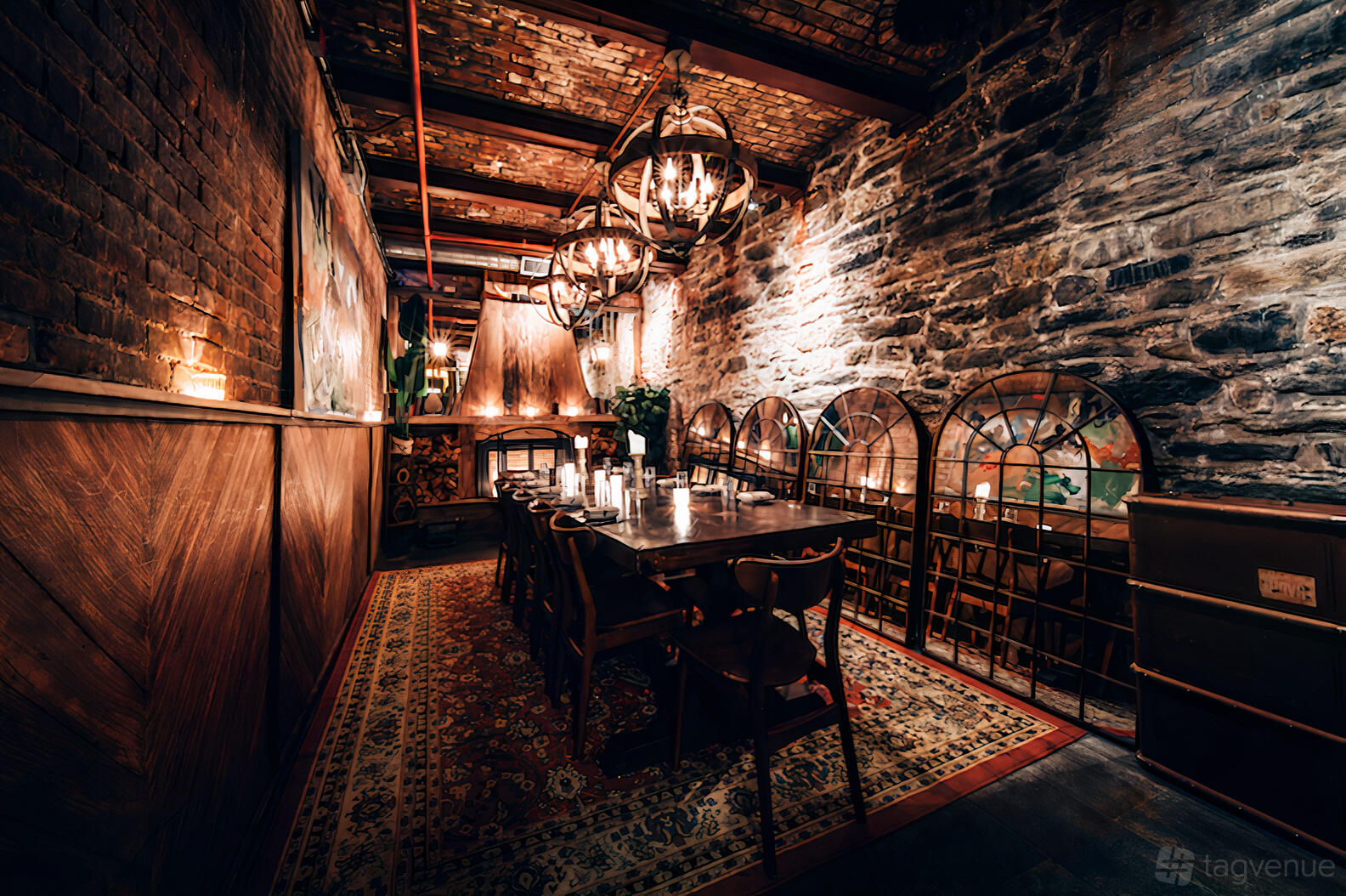 A dining room with exposed brick walls, wooden beams, chandeliers, and a long table set with candles at Gelso & Grand.