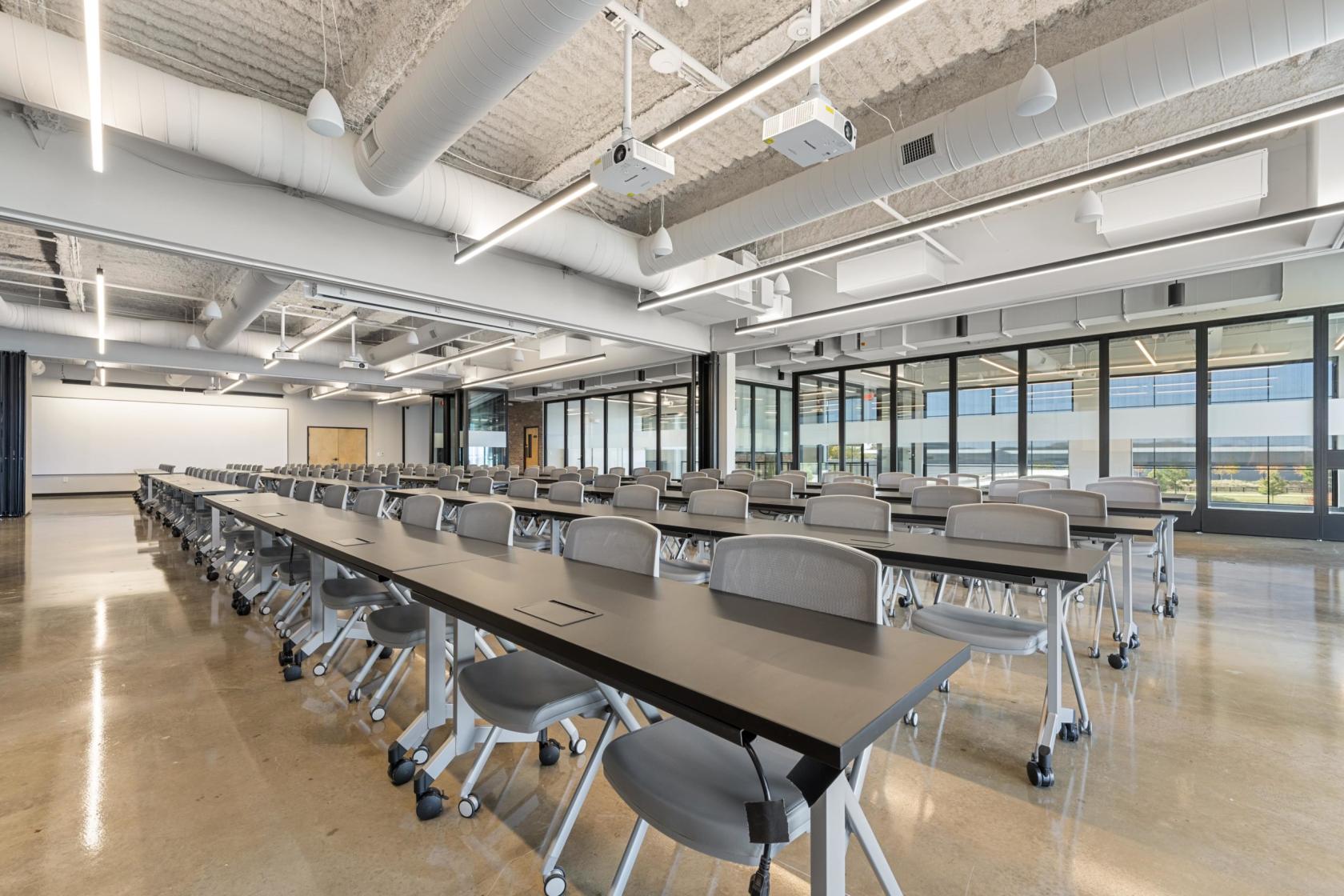 A training room with rows of black tables, gray chairs, polished floors, and floor-to-ceiling windows at ROAM AT TRILITH.