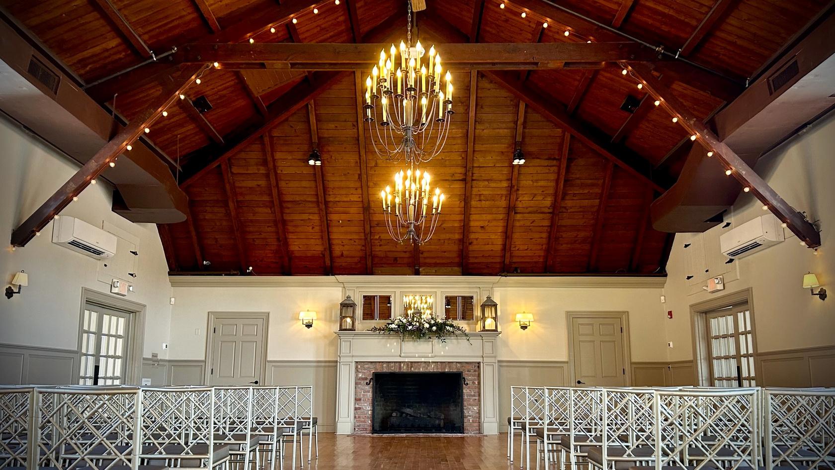 An indoor event space with vaulted wood ceilings, chandeliers, and a brick fireplace at The Old Field Club.