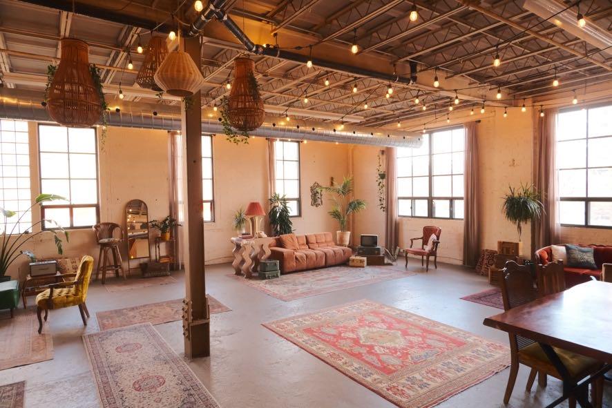 A loft with exposed ceilings, string lights, vintage furniture, and large windows at Junto Studio.