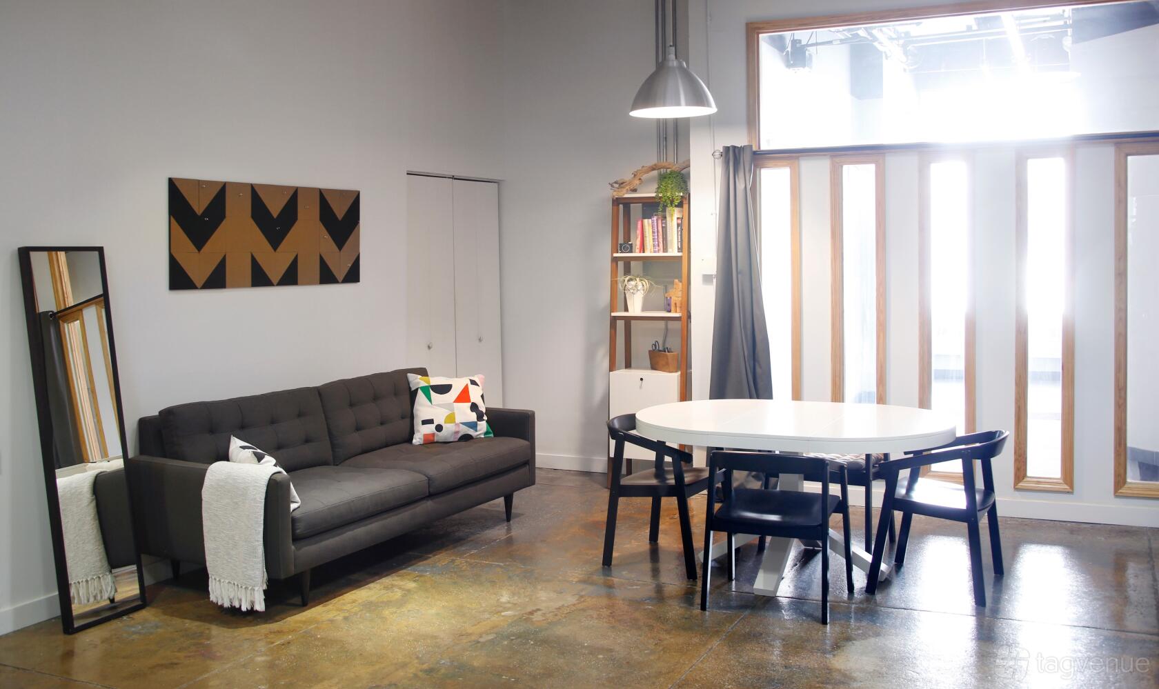 A dance studio with polished concrete floors, a gray sofa, round table with black chairs, and floor-to-ceiling windows at Christine's Studio.