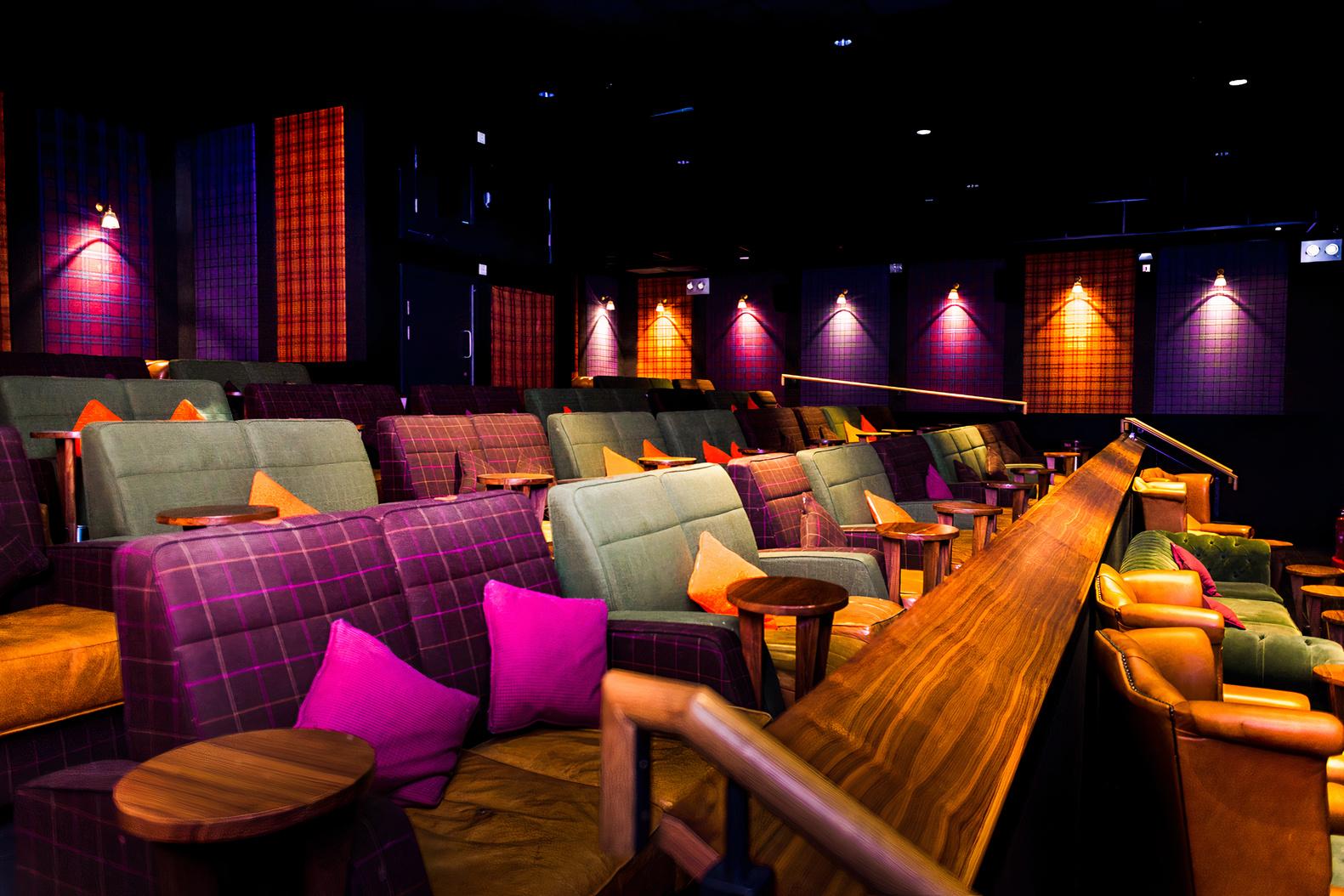 An auditorium with plush armchairs, colorful cushions, and wood side tables at Everyman Leeds