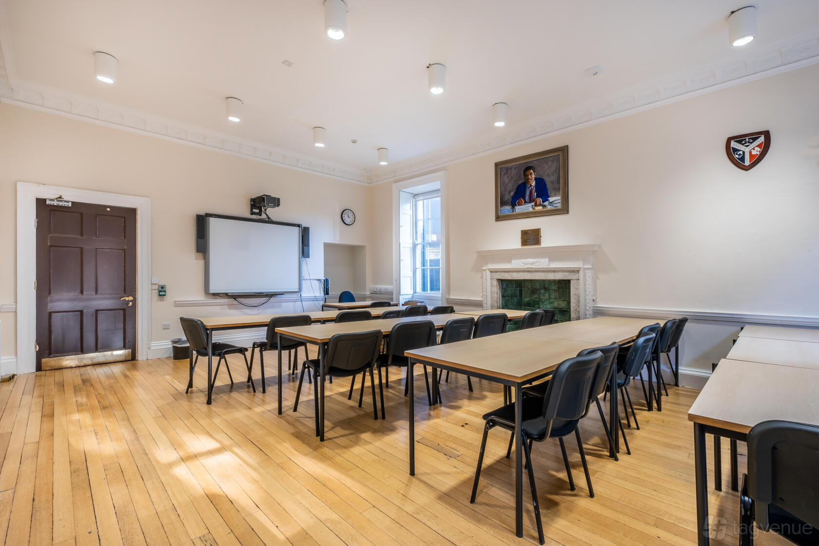 A training room with wooden floors, rectangular tables, black chairs, a whiteboard, and a fireplace at Ruskin Venues.