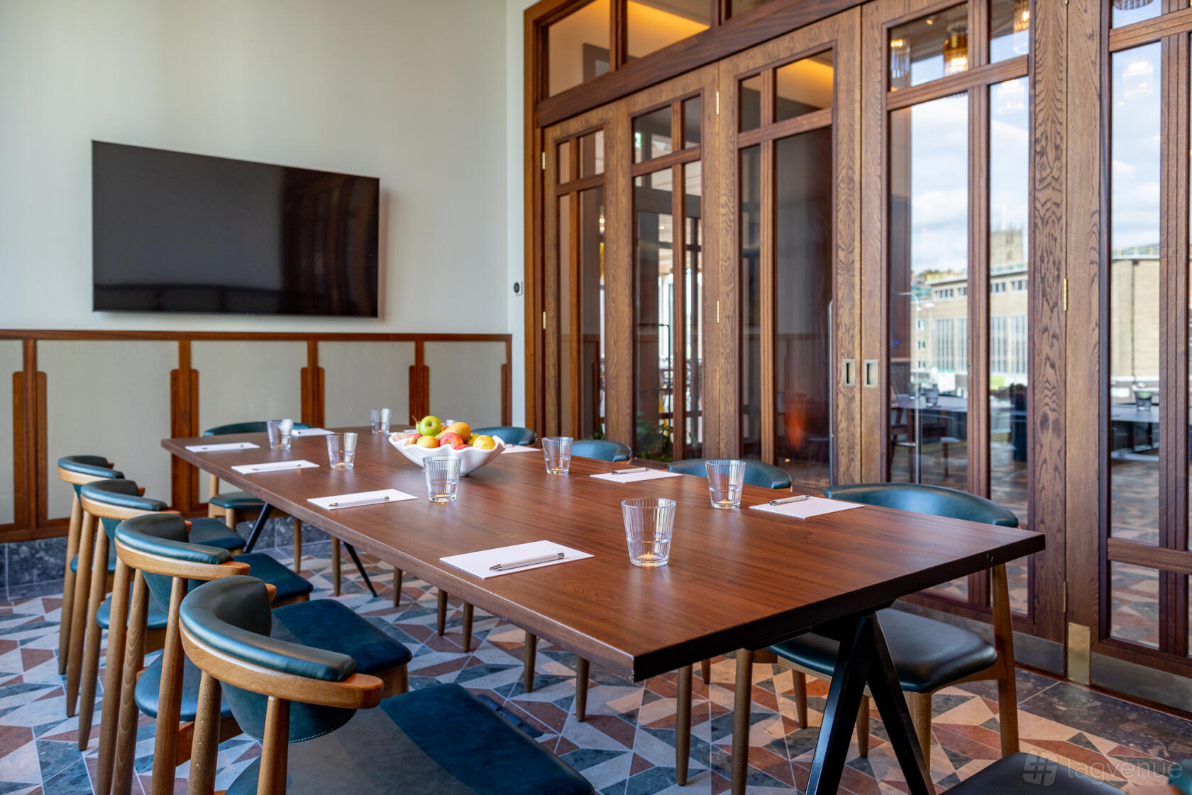A boardroom with a long wooden table, modern chairs, glass tumblers, notepads, and a wall-mounted screen at Cleaver & Wake.