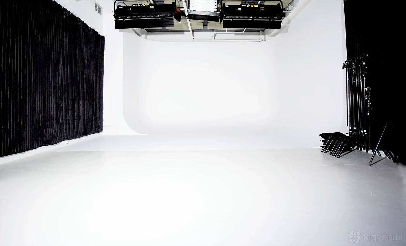 A soundstage with a white cyclorama wall, black curtains, and overhead lighting at Blonde + Co.