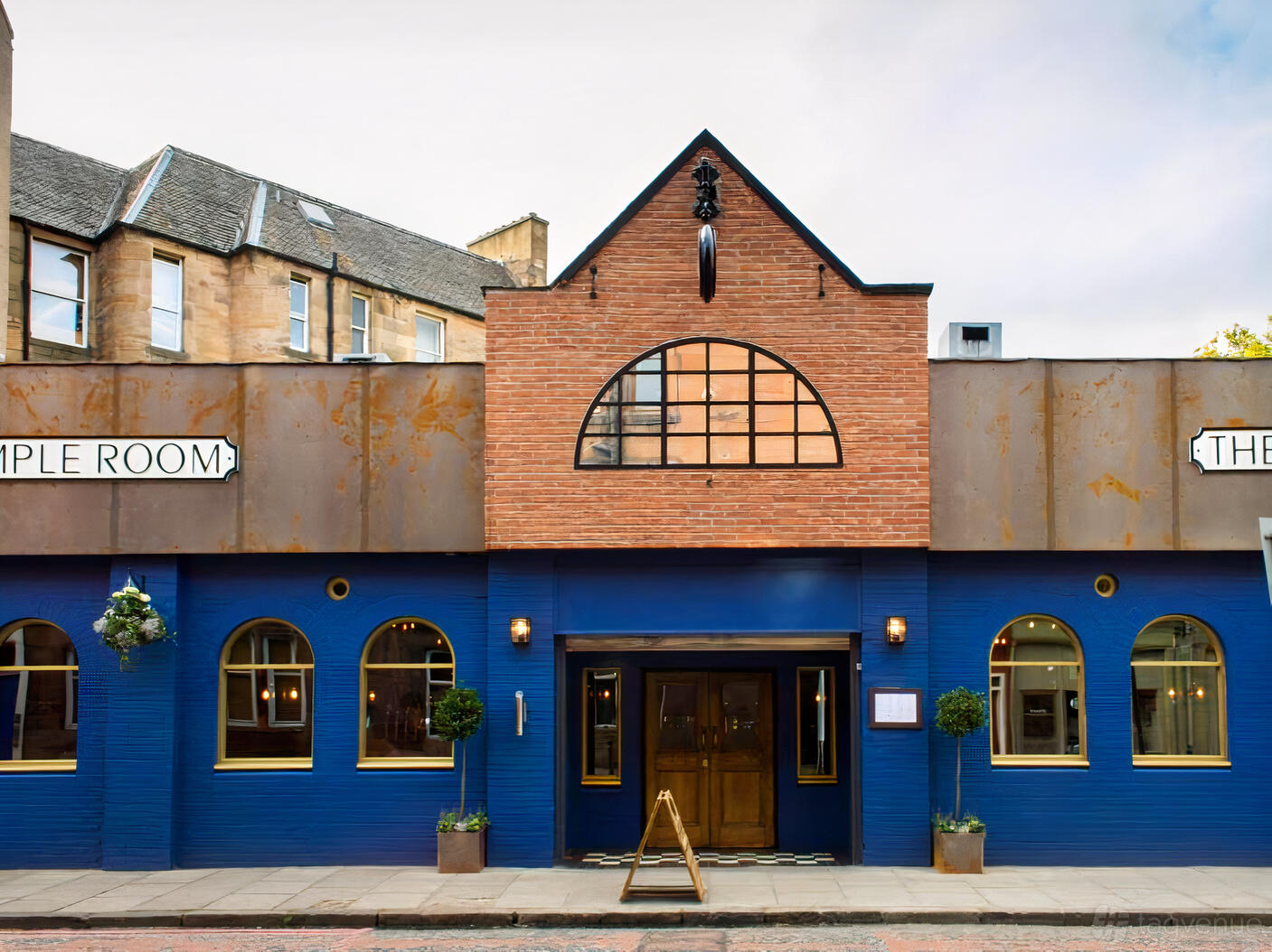 A pub bar with a blue and brick facade, arched windows, and wooden entrance doors at Caley Sample Room.