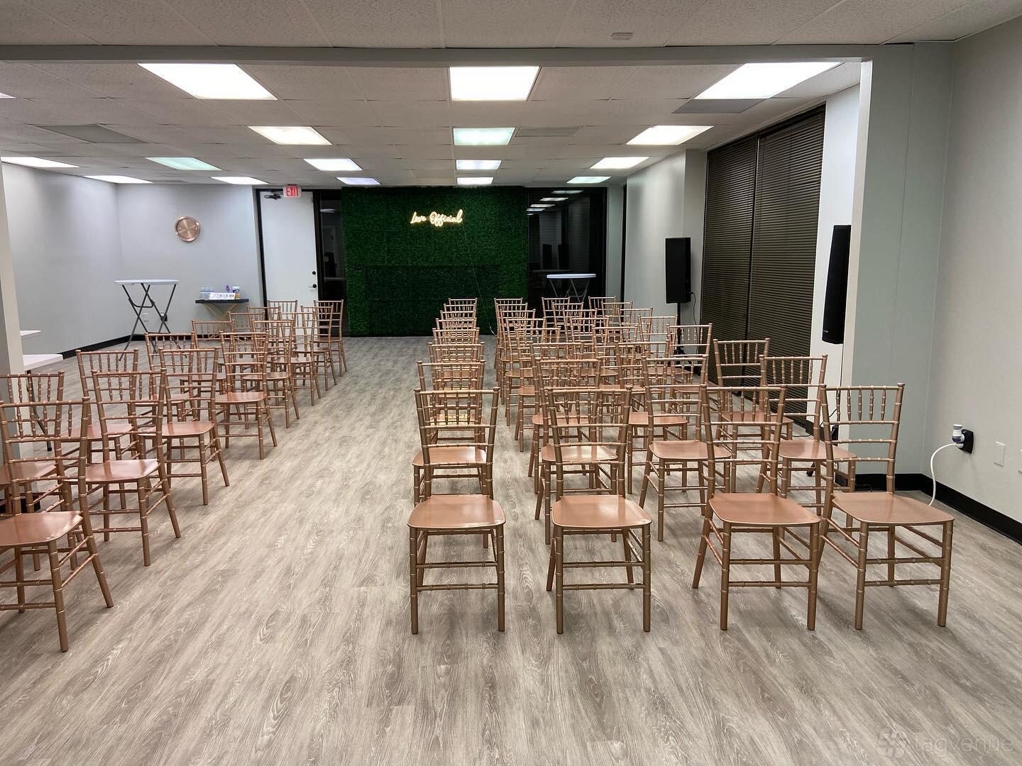 An event venue with gold chairs in rows, wood flooring, and a green accent wall at Love Official.