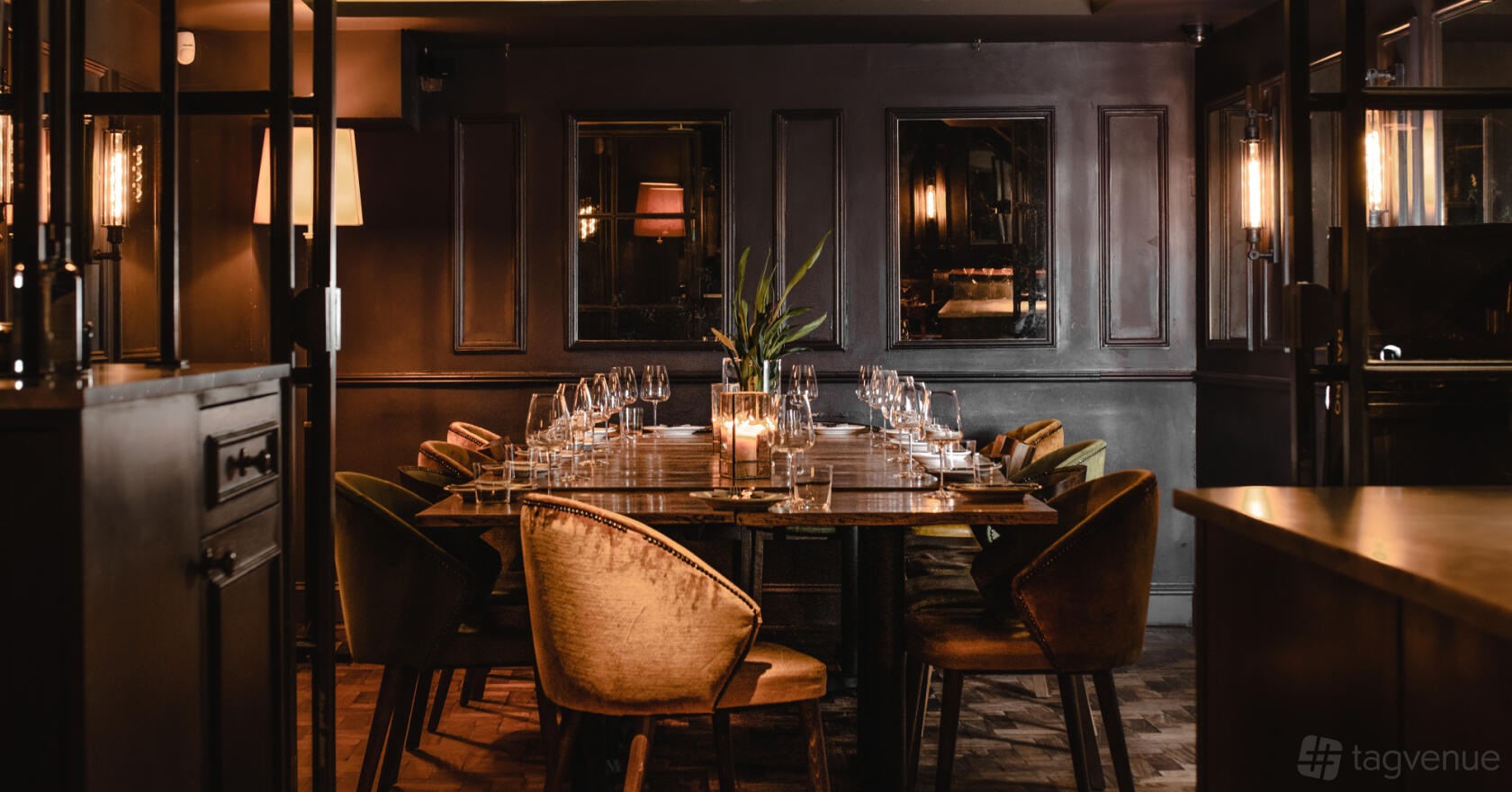 A restaurant dining room with velvet chairs, candlelit table settings, and dark paneled walls at Ember Yard.