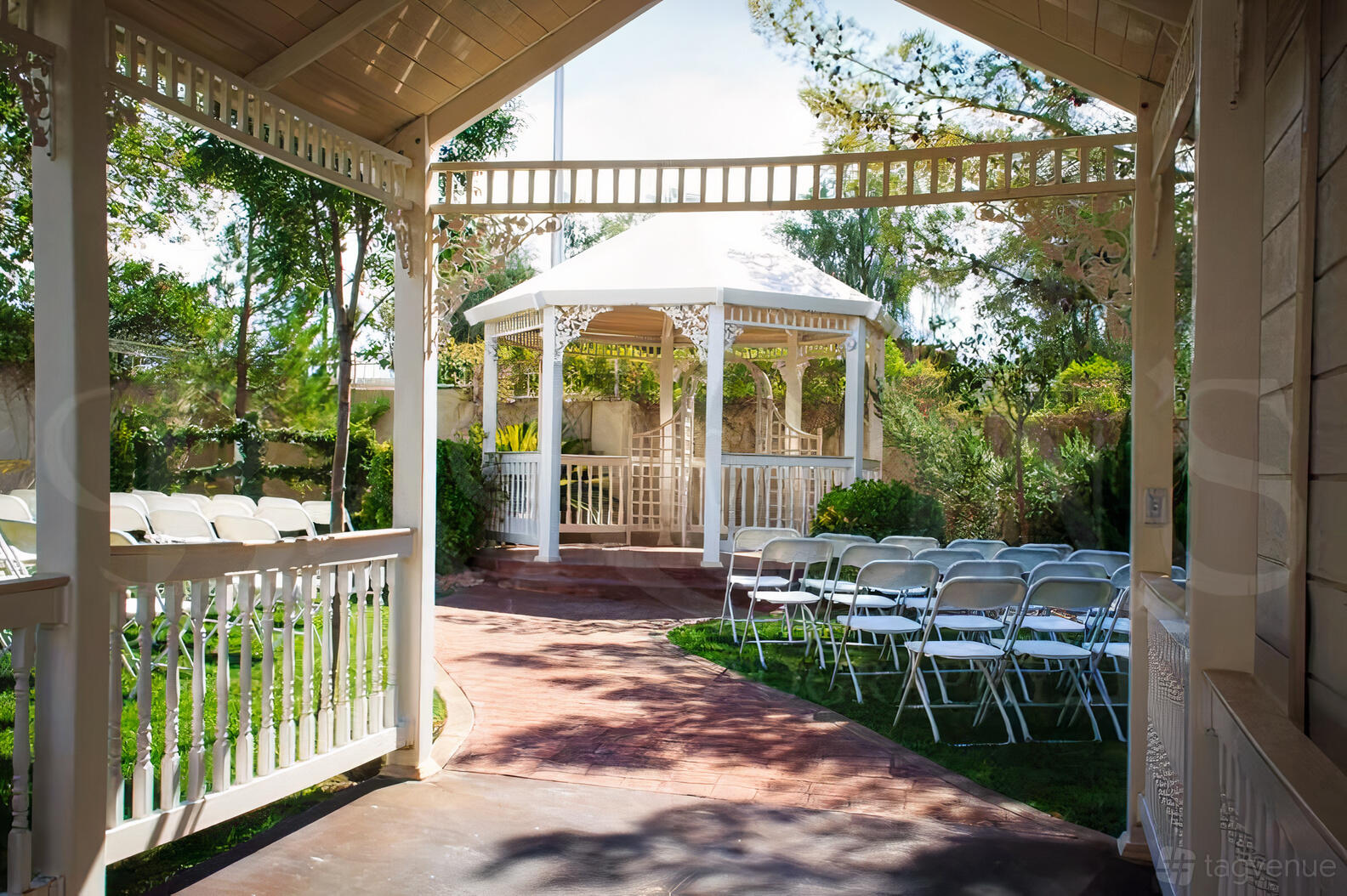 An outdoor chapel area with a white gazebo, folding chairs, and landscaped gardens at Little Chapel on the Corner.