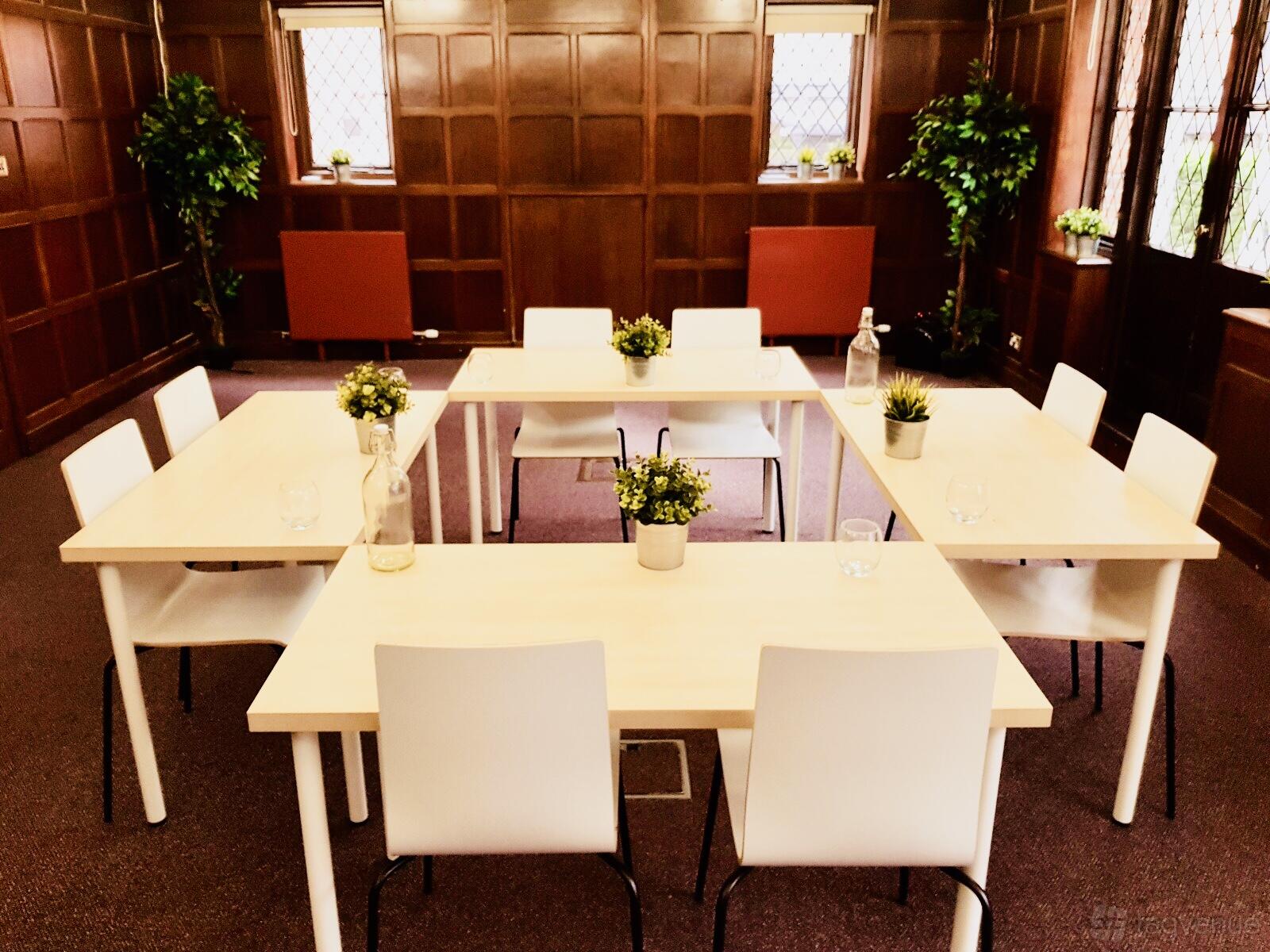 A meeting room with wooden paneled walls, white tables arranged in a U-shape, and potted plants at Rivertech.